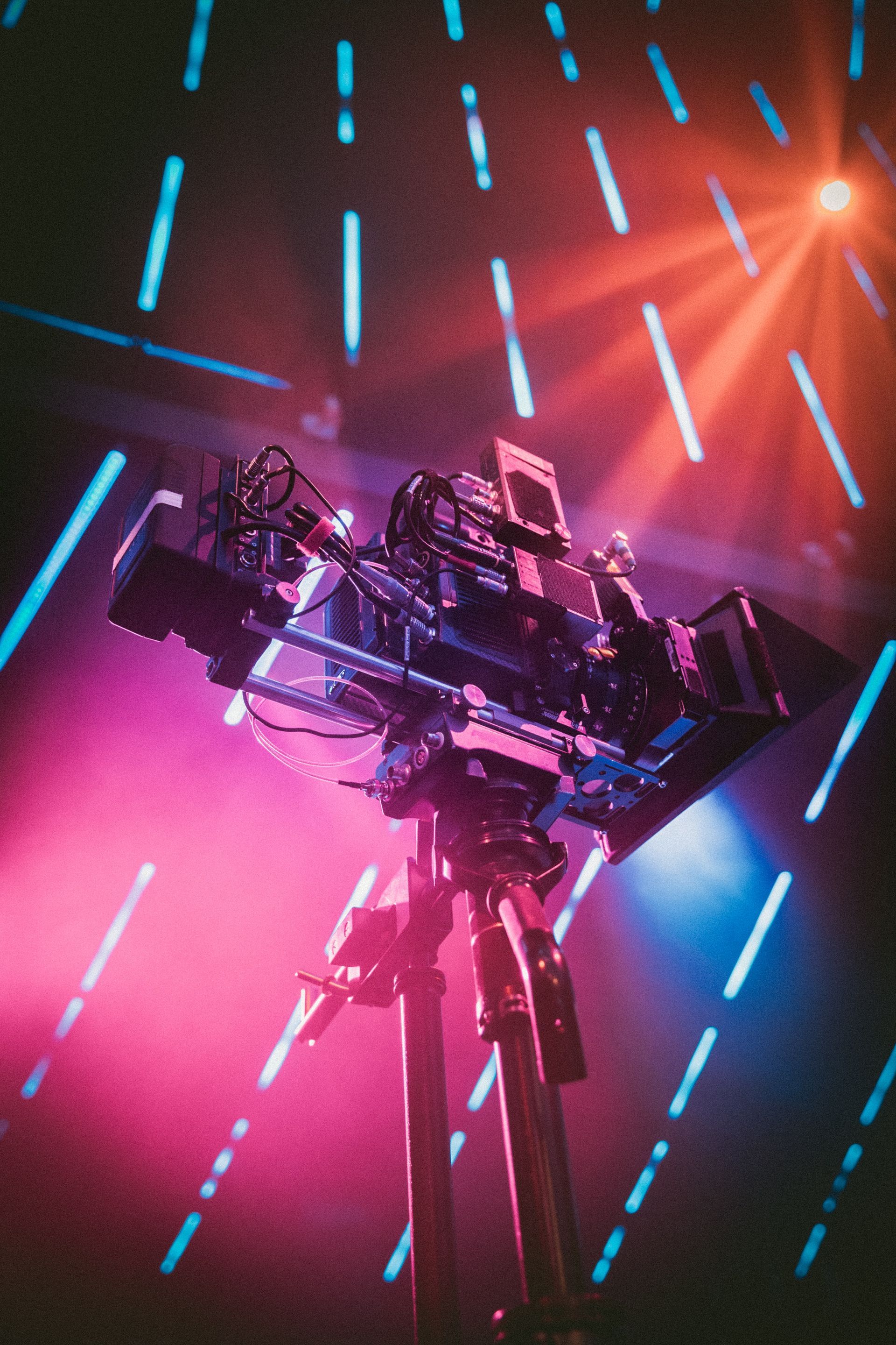 A camera on a tripod with purple and blue lights behind it.