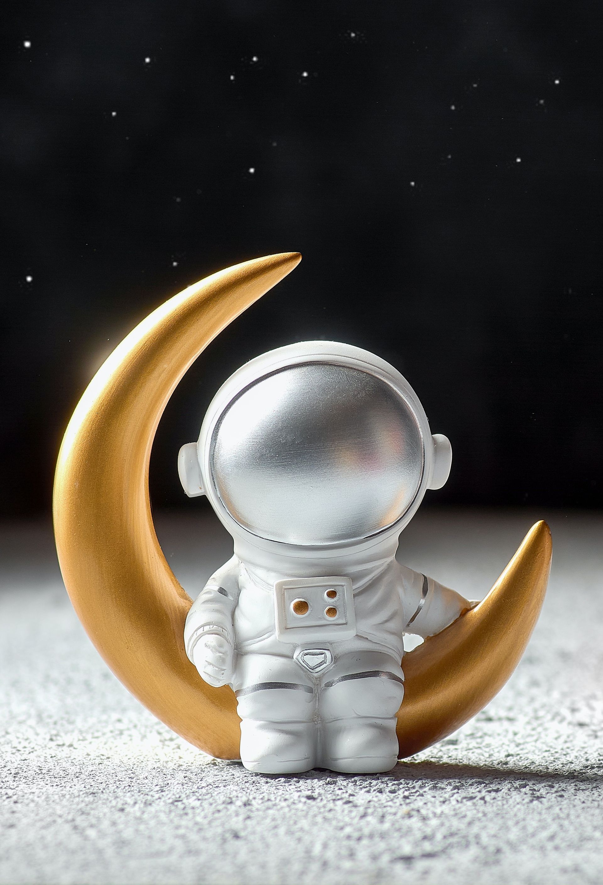 A figurine of an astronaut sitting on a gold crescent moon.