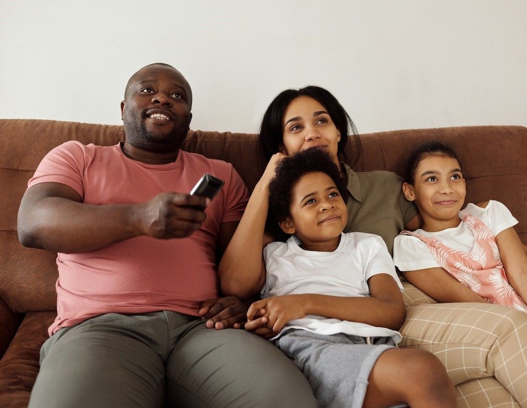 A family is sitting on a couch watching tv.
