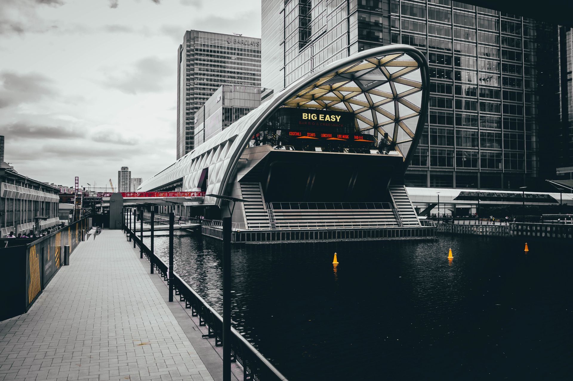 A black and white photo of a building in Canary Wharf next to a body of water.