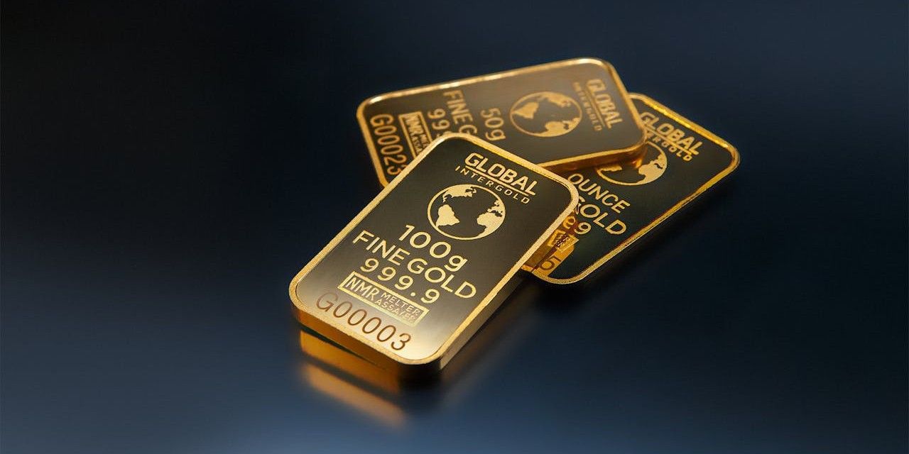 Three gold bars on a dark, reflective surface. Each bar is marked 