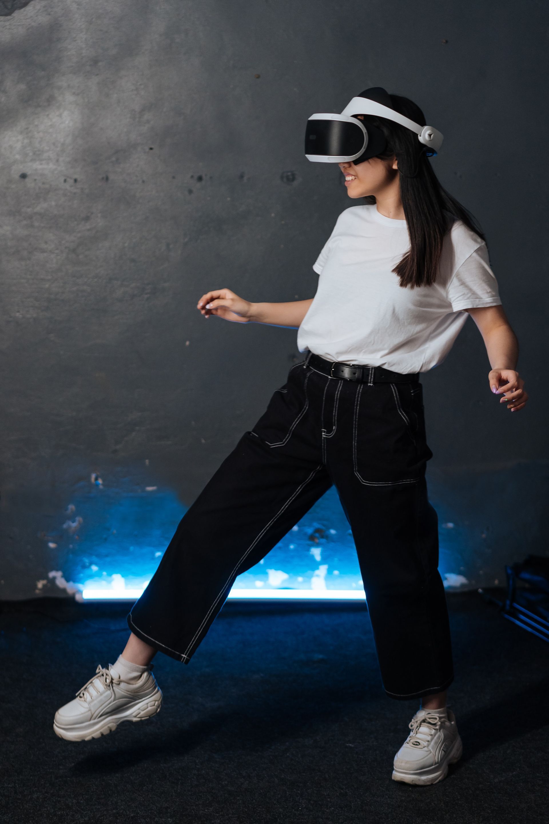 A woman wearing a virtual reality headset is dancing in a dark room.