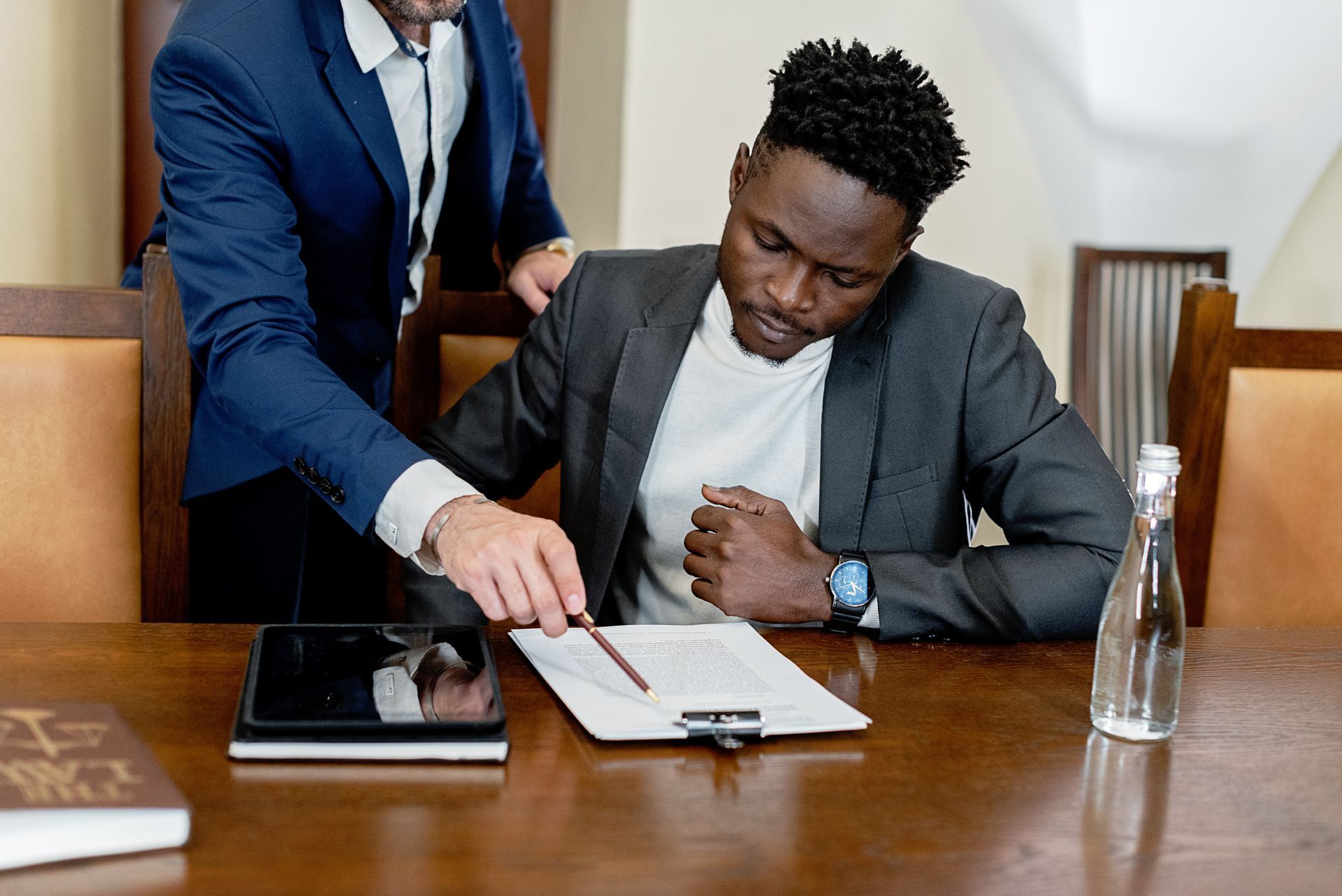 Two men are sitting at a table looking at a tablet.
