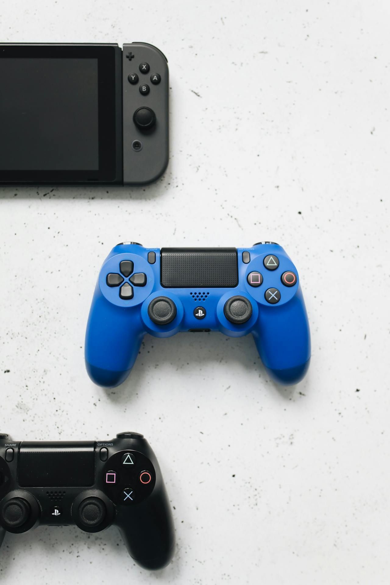 A Nintendo Switch , a ps4 controller , and a cell phone are on a table.