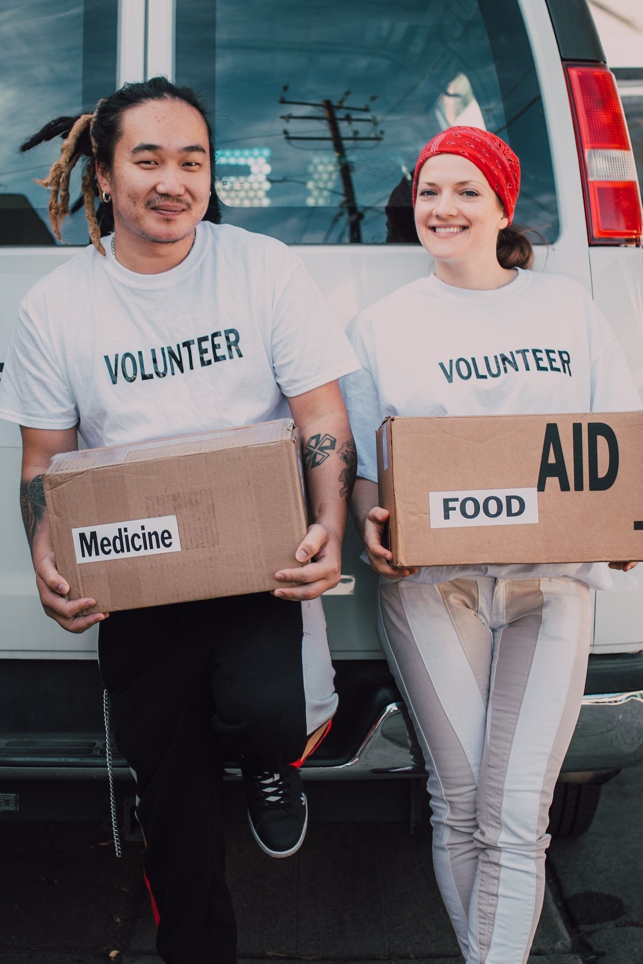 A man and a woman are holding boxes in front of a van.