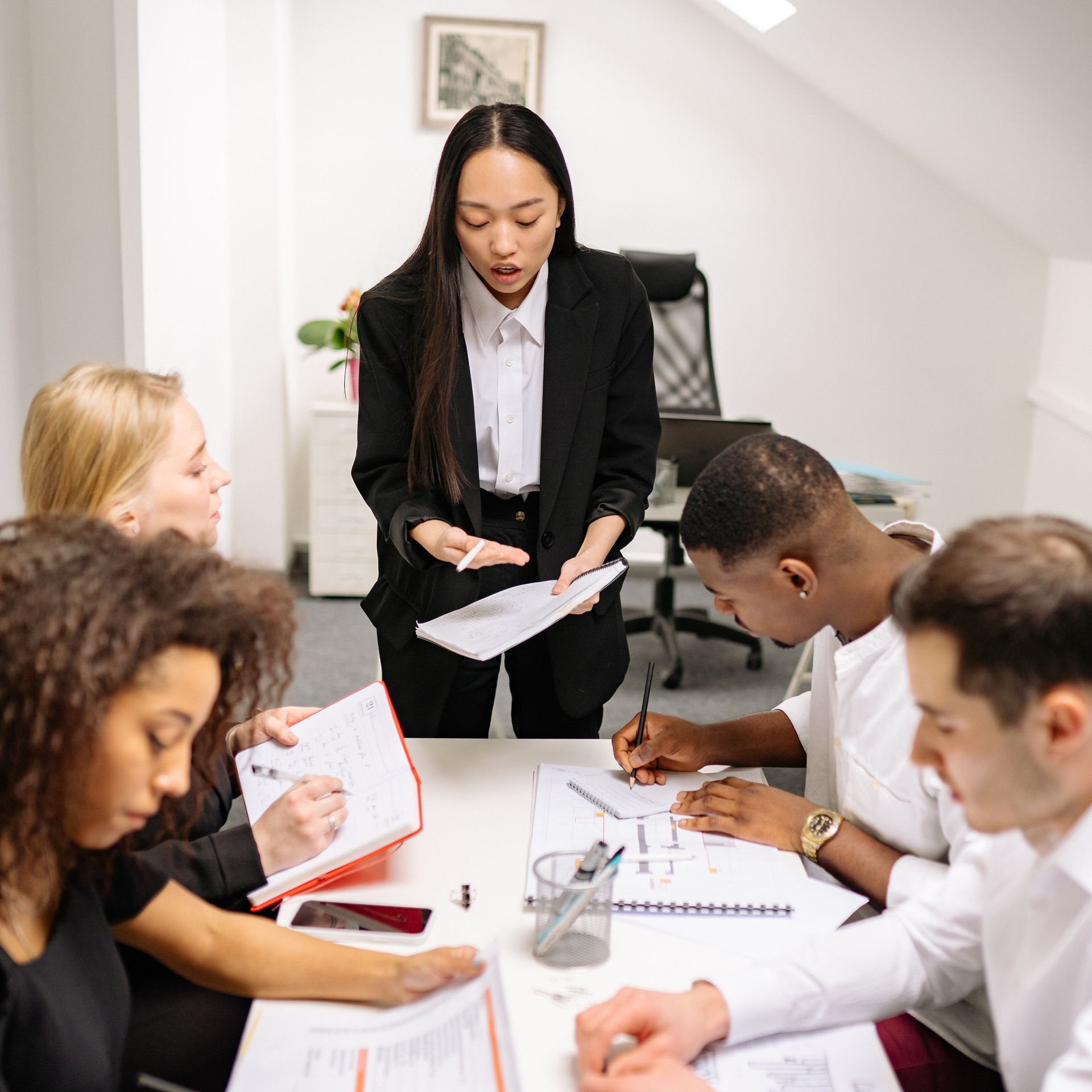 A group of people are sitting around a table and a woman is giving a presentation