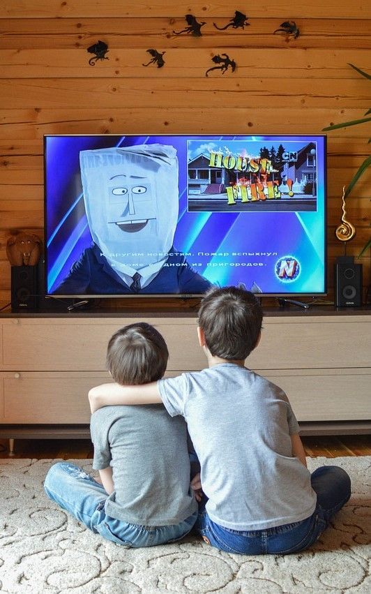 Two boys are sitting on the floor watching a television.