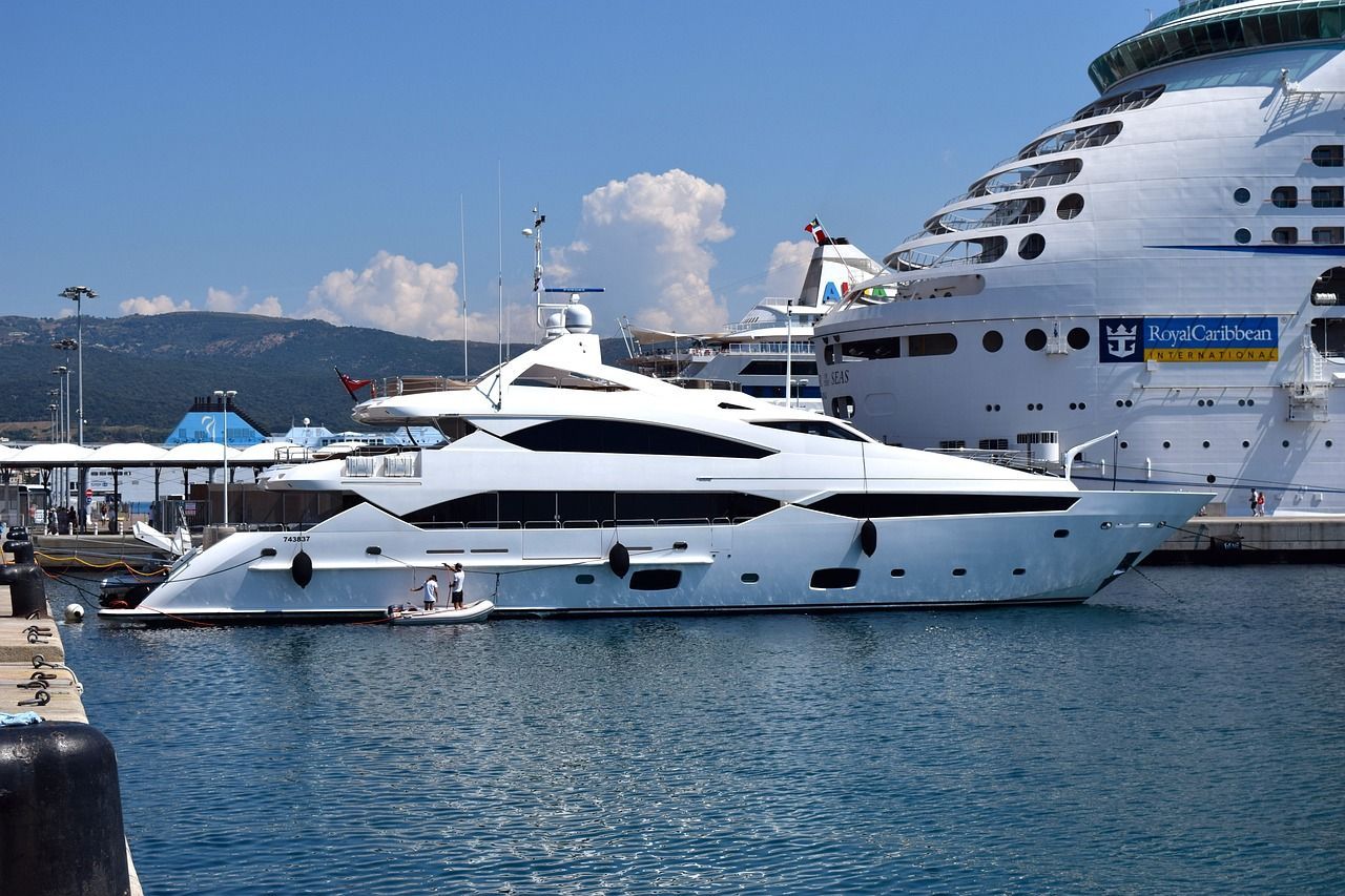 A large white yacht is docked in a harbour next to a cruise ship.