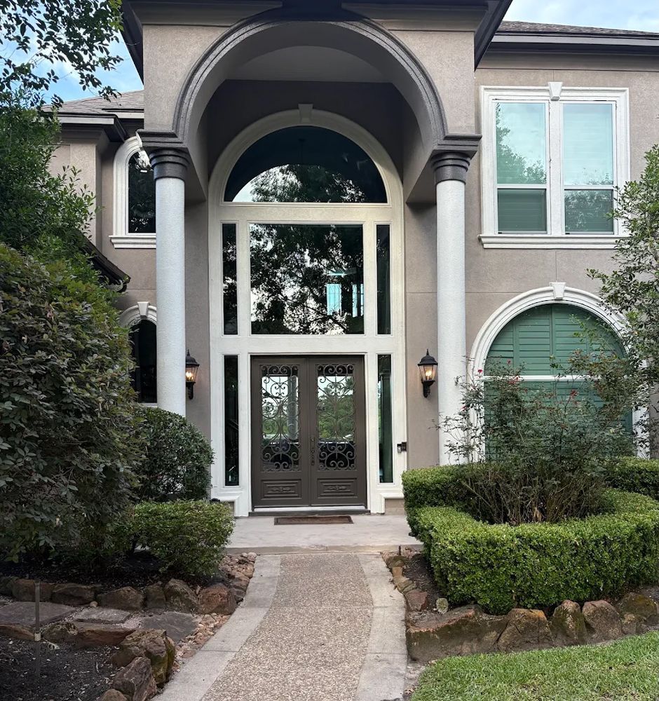 A modern two-story suburban home with a concrete walkway leading to a double-door entrance under a large arched portico.