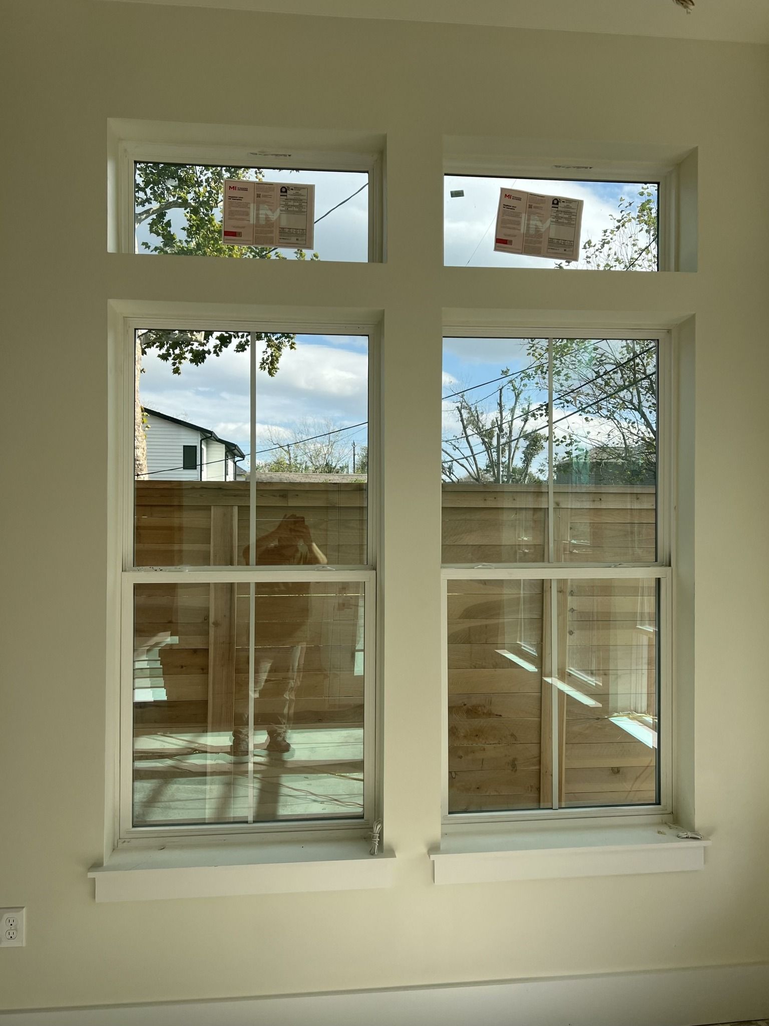 Two white, double-hung windows with fixed transom windows above, set into a plain, off-white interior wall.