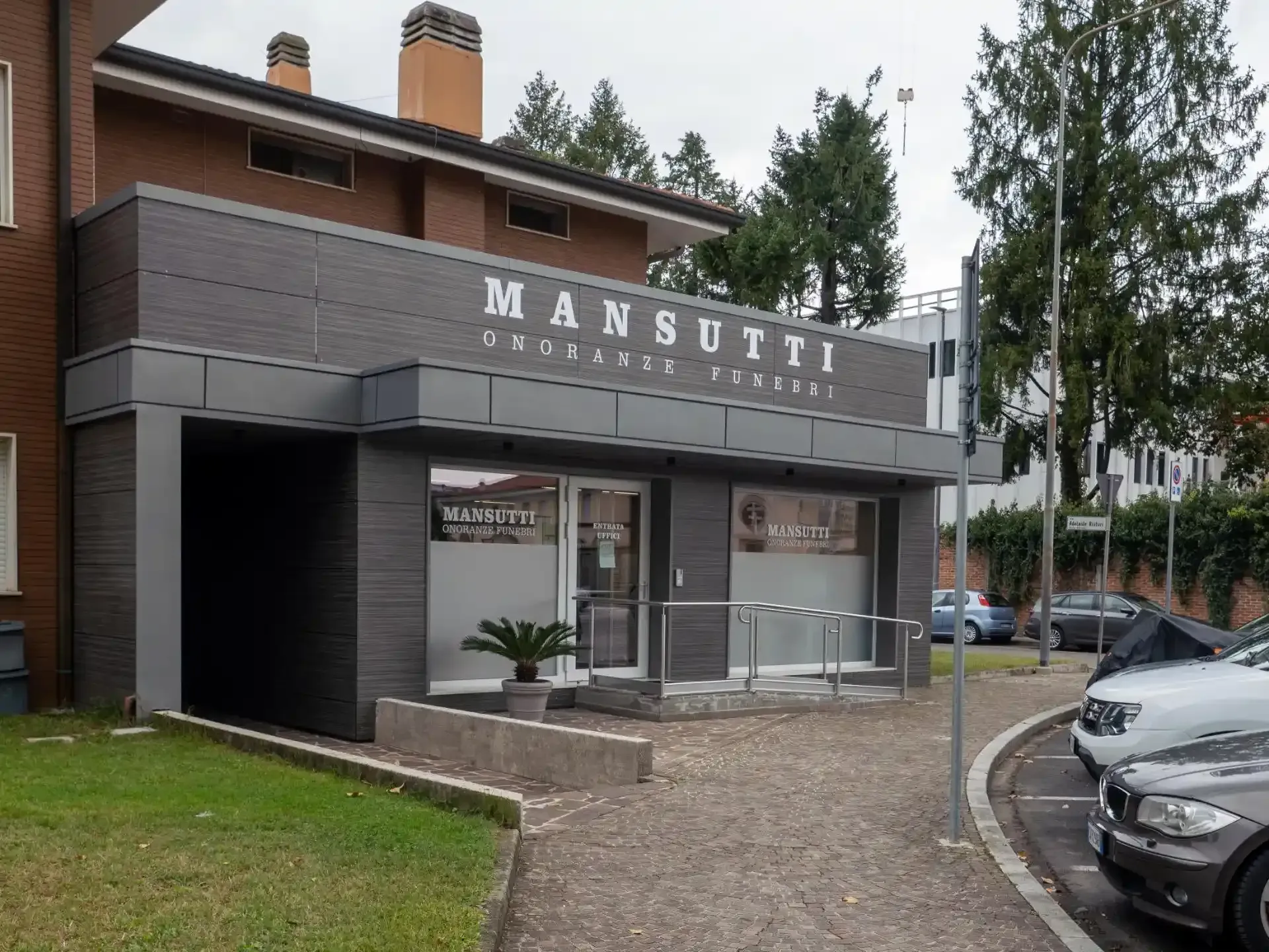 Edificio per uffici Mansutti con facciata, insegna e area d'ingresso grigio scuro.