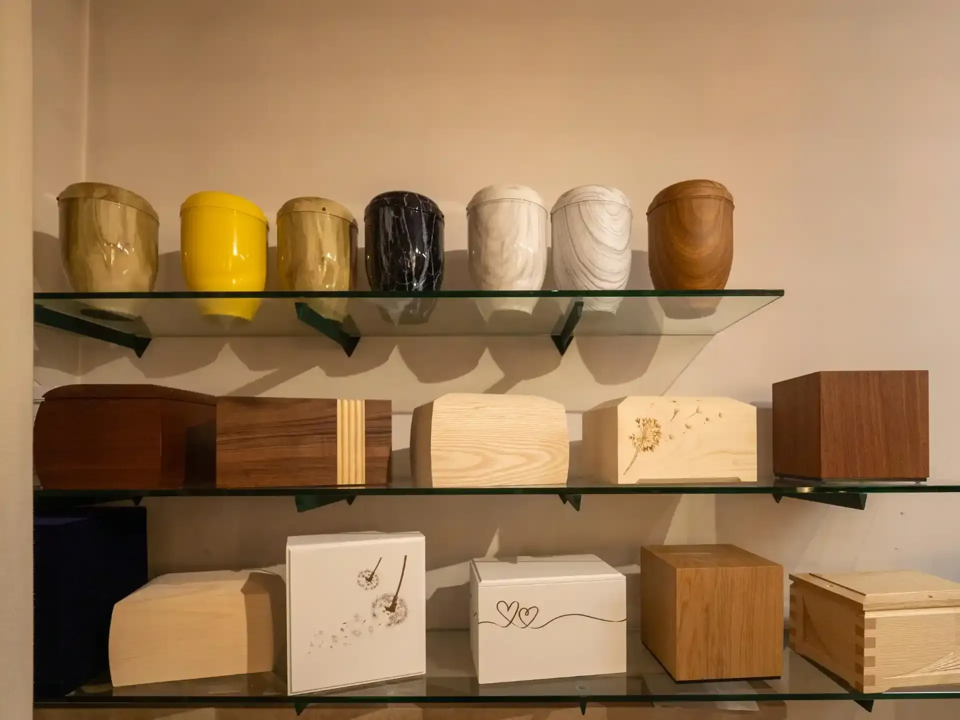 Scaffali che espongono varie urne per le ceneri in un'agenzia di pompe funebri; finiture in legno, ceramica e metallo.