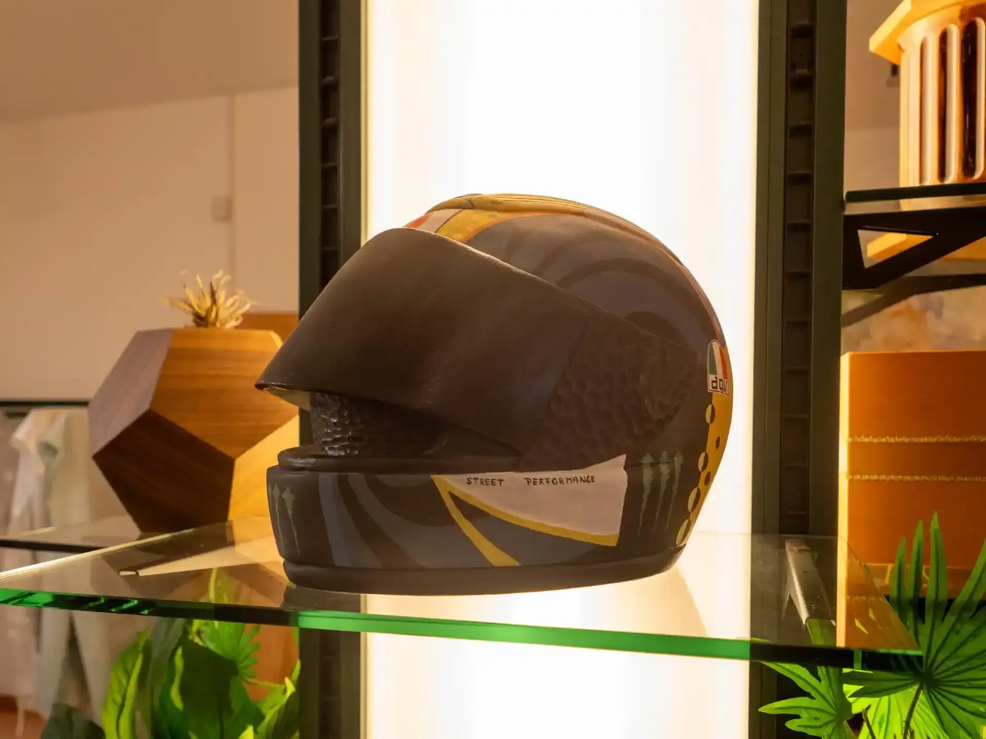 Casco da motociclista nero e oro su una mensola di vetro.