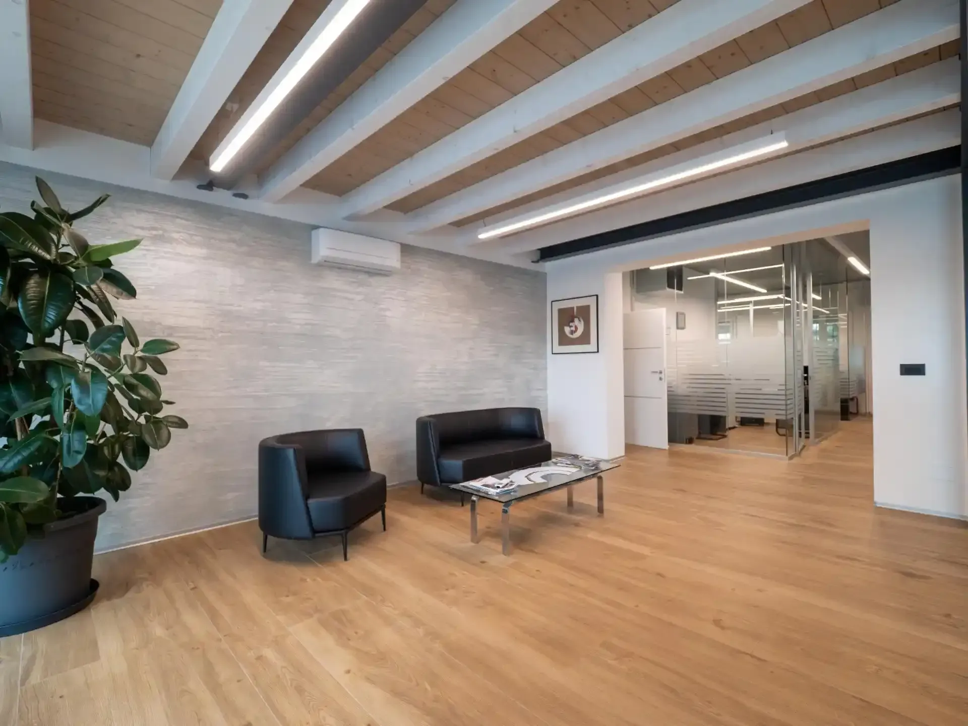 Sala d'attesa con sedie in pelle nera, tavolino, pianta in vaso e pavimenti in legno chiaro.