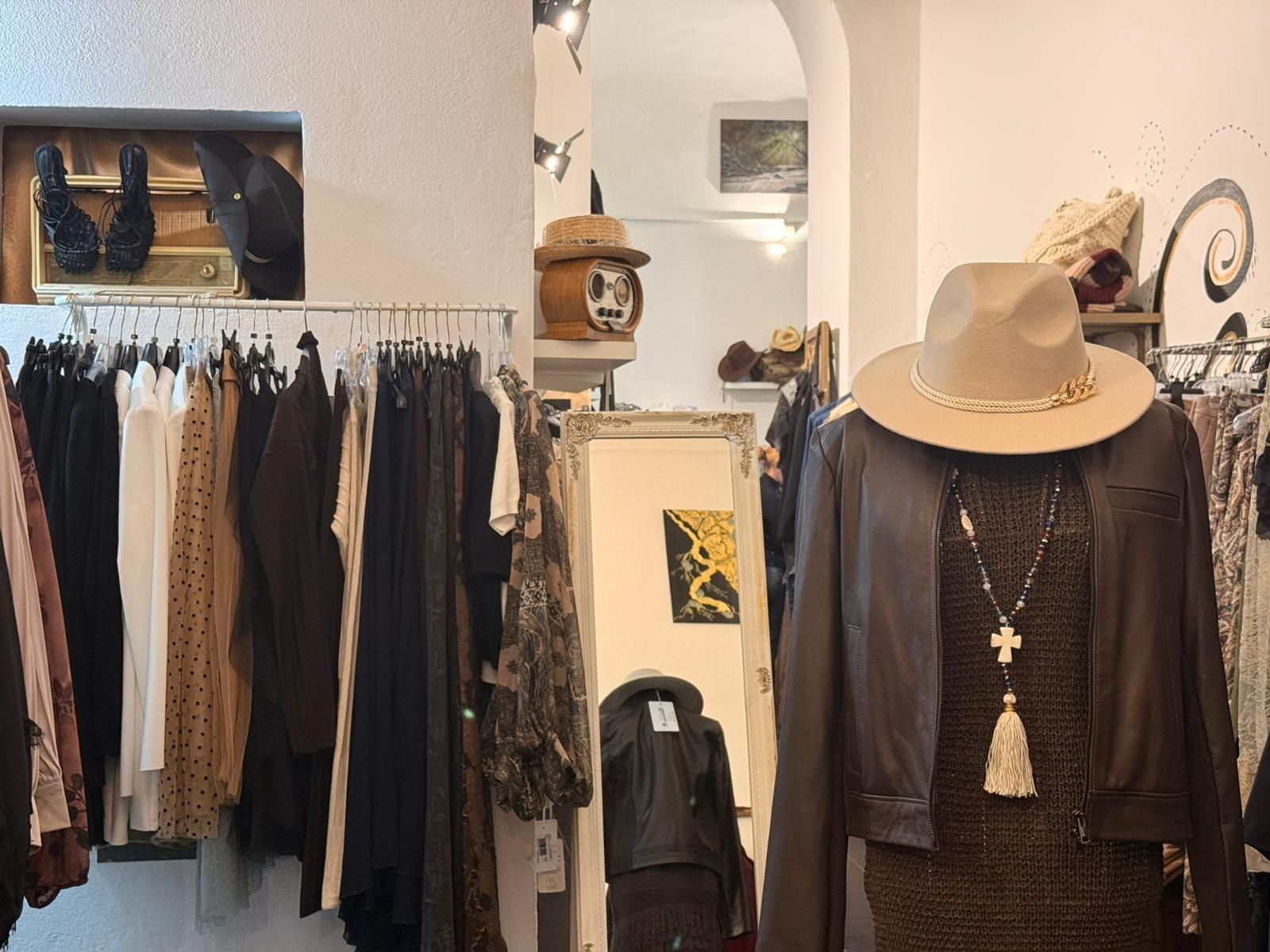 Interno di un negozio di abbigliamento con appendiabiti e un manichino che indossa un cappello e una giacca.