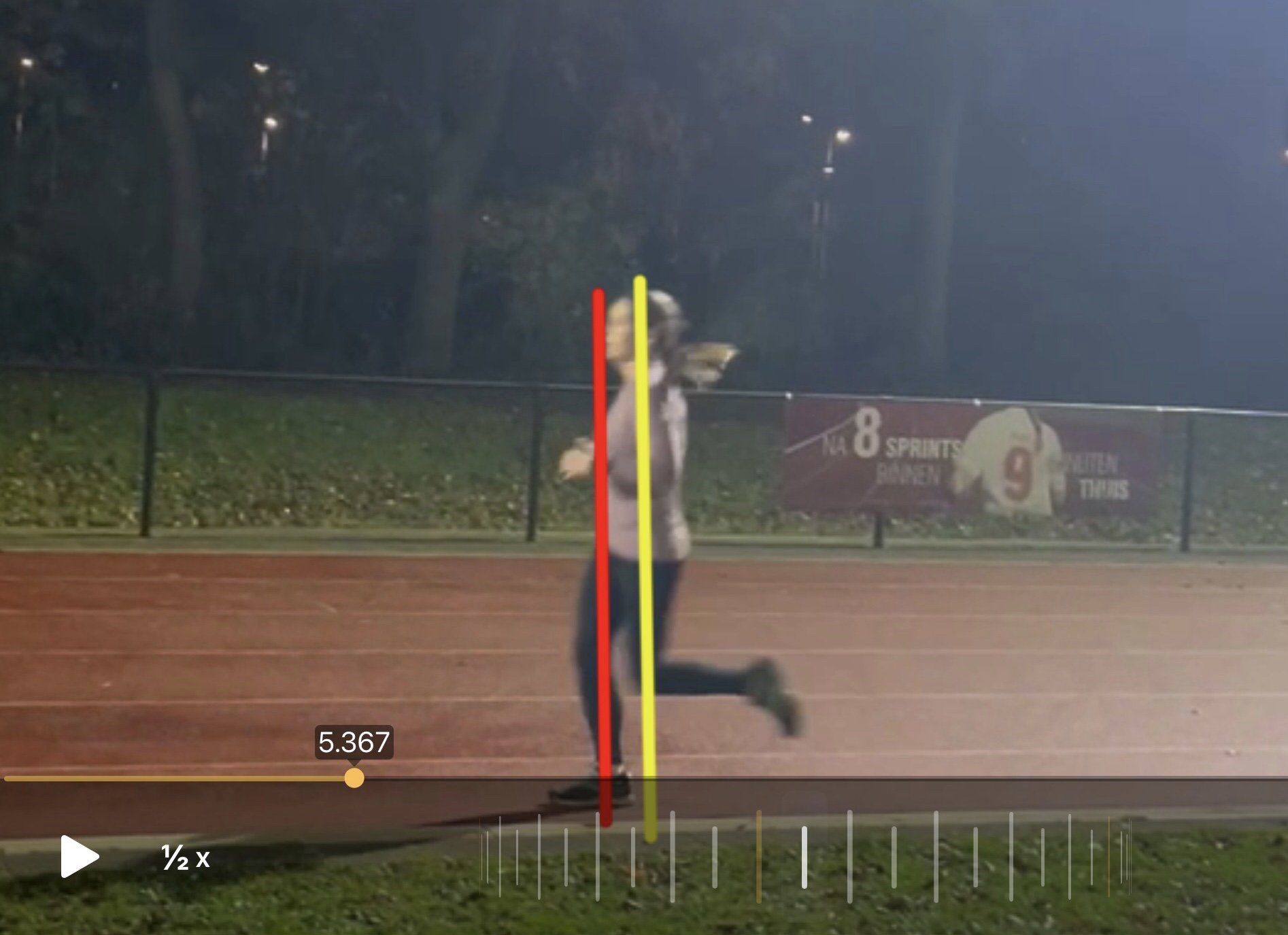 Hardloper op een atletiekbaan met gele en rode lijnen, nachtelijke setting.
