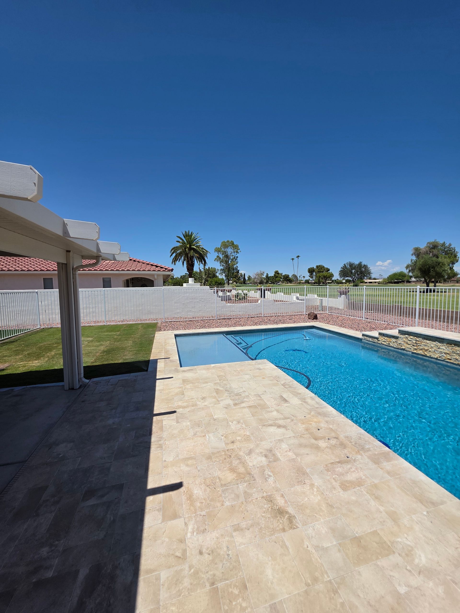 A backyard with a blue pool, hot tub, and patio under a clear, blue sky. A white pergola and green grass are visible.