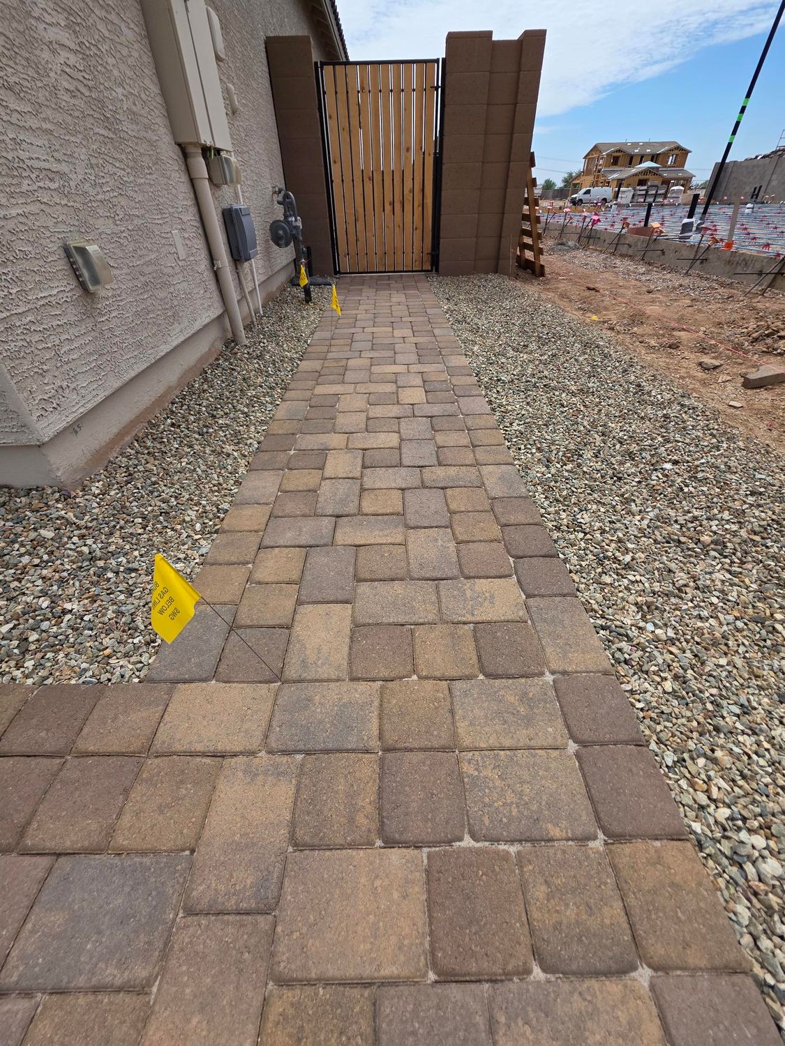 Paver walkway leading to a wooden gate; gravel on either side; new construction setting.