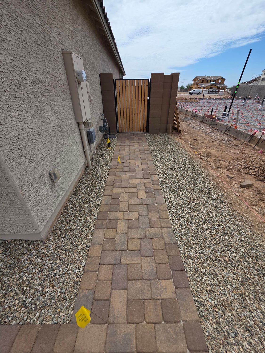 Brick pathway leading to wooden gate; gravel borders. Side of house on left, construction site on right.