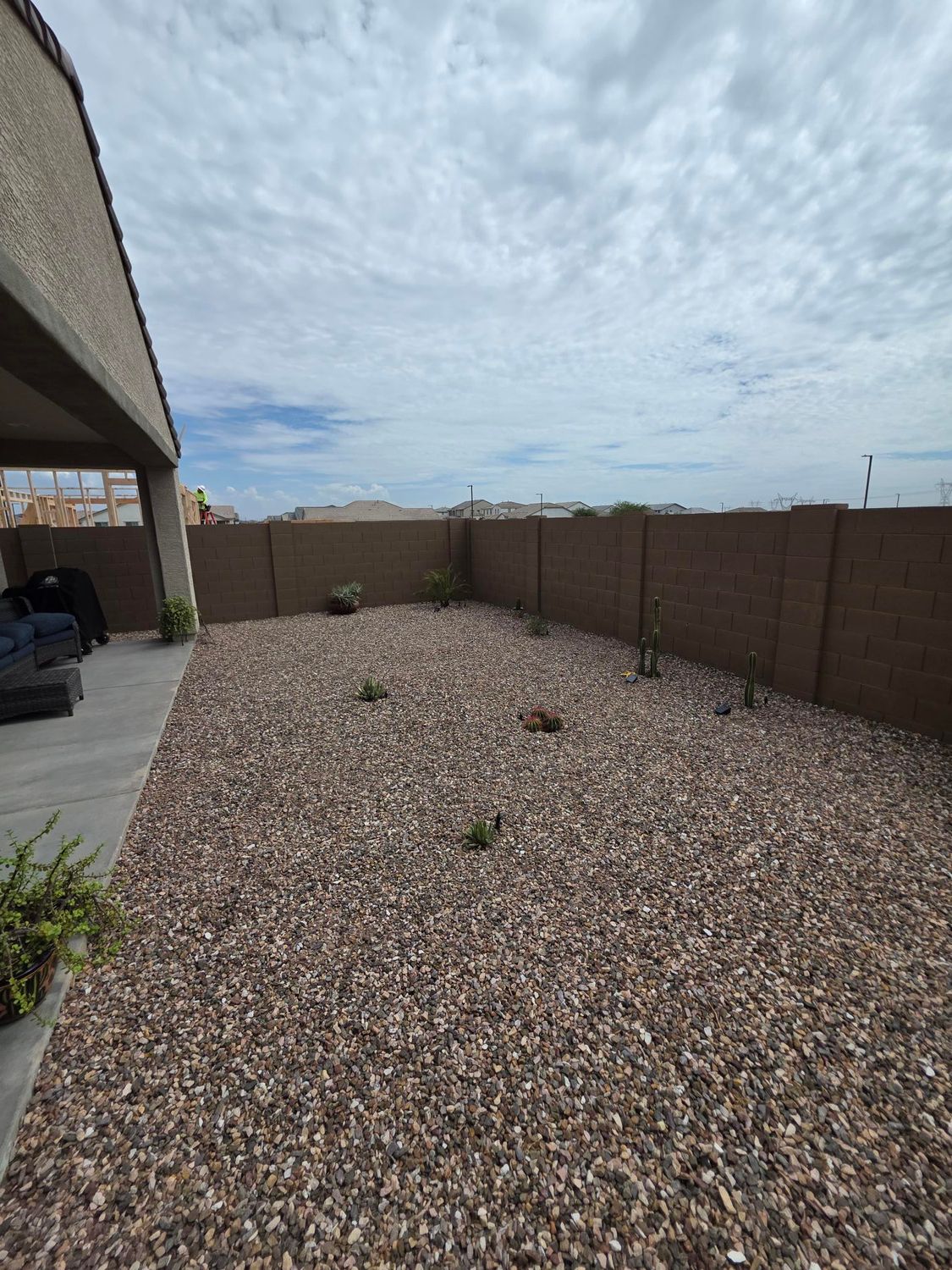 Gravel backyard with a low wall, covered patio, and cloudy sky overhead.