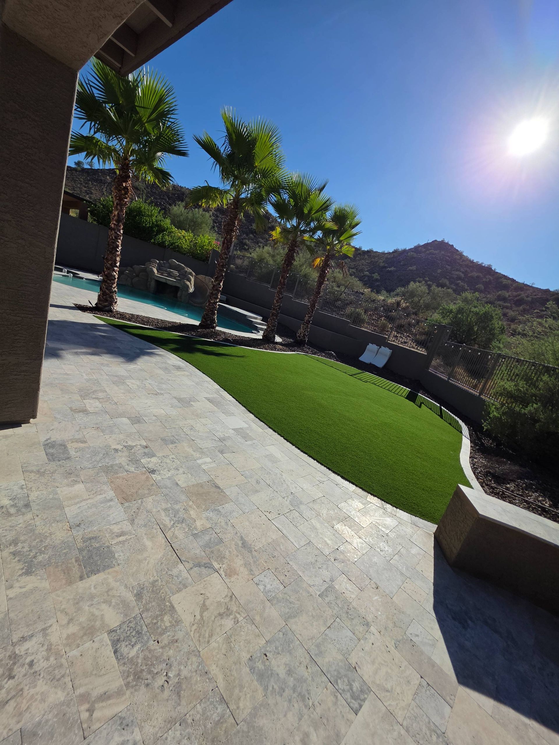 Backyard with palm trees, artificial grass, and a pool, mountains in the background. Sunny day.