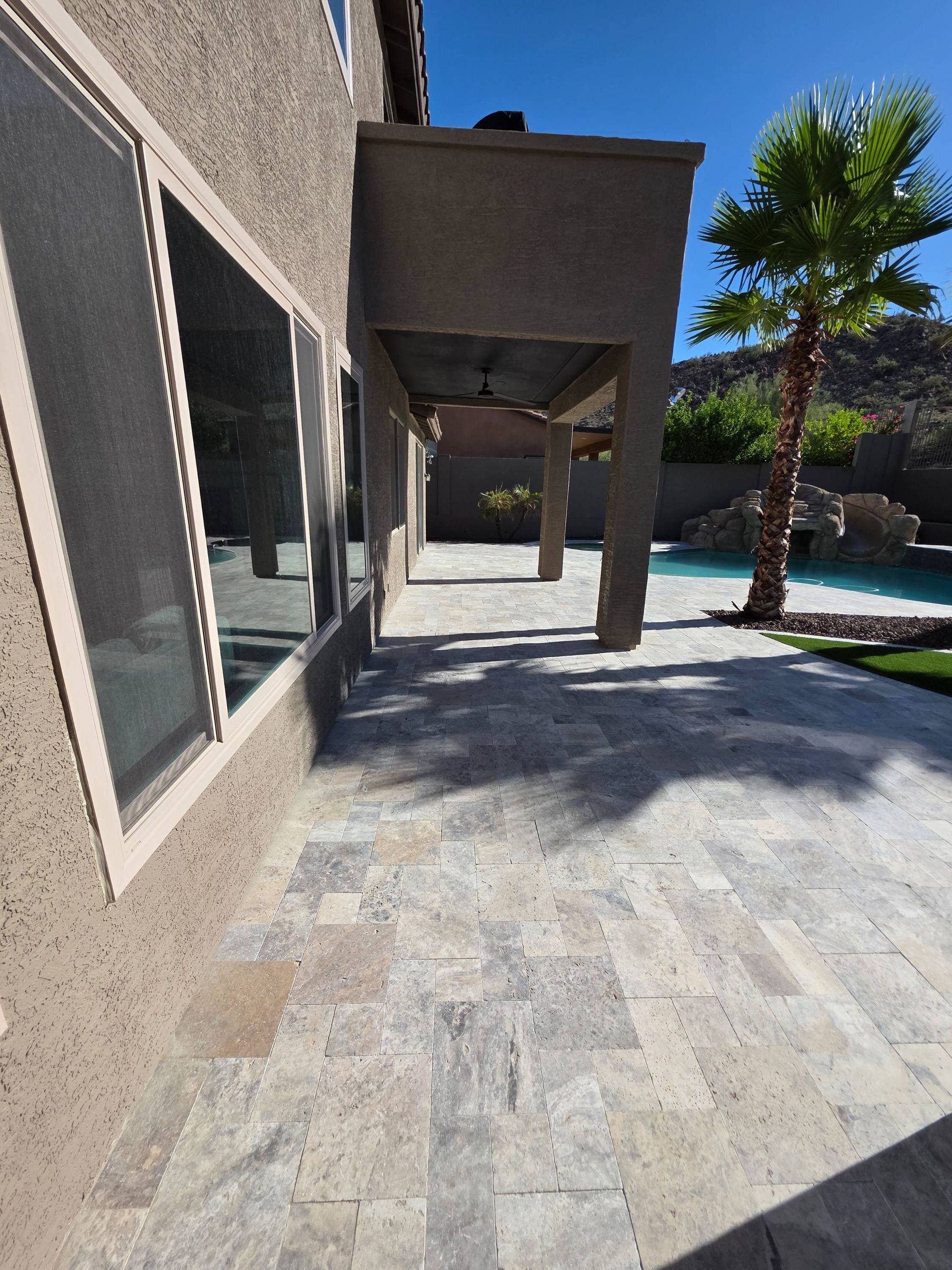 Exterior view of a house with a stone patio, covered porch, and swimming pool.