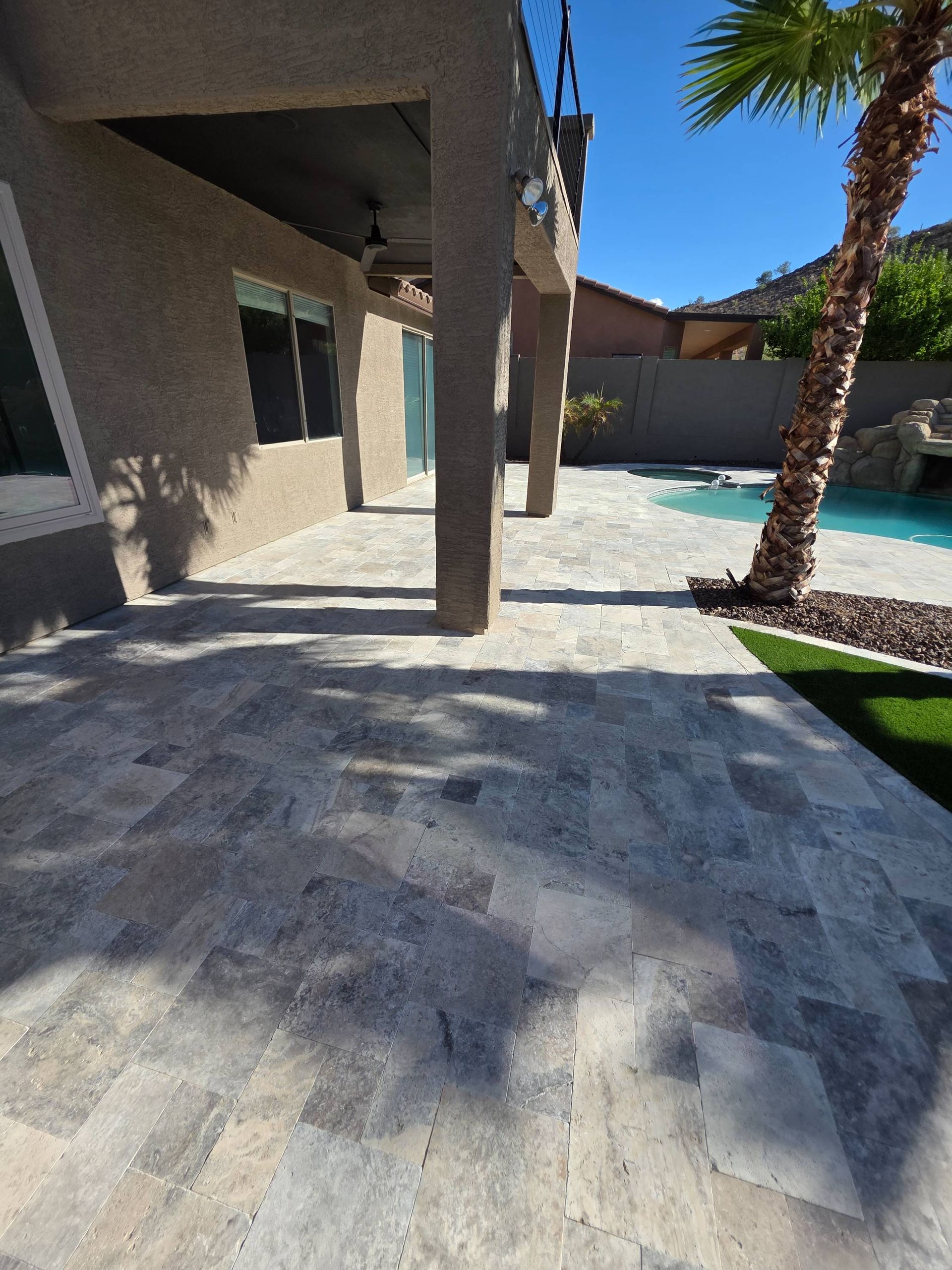 Patio with light gray tile, columns, and a view of a pool with a palm tree and blue water.