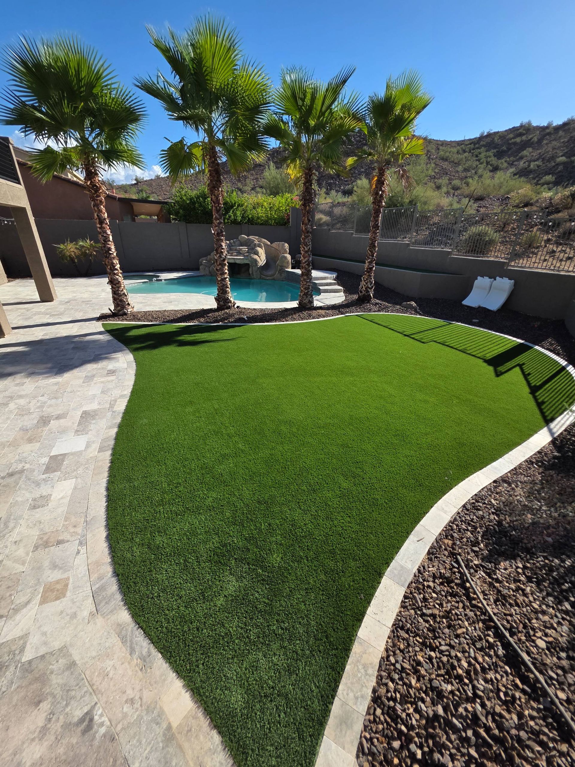 Lush green artificial turf in a backyard with a pool and palm trees.