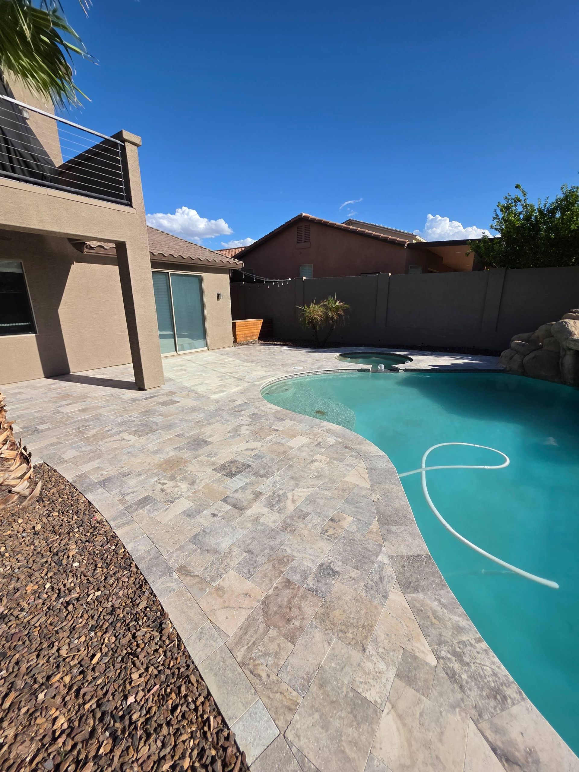 Swimming pool with stone patio, blue water, tan and brown stone, and blue sky.