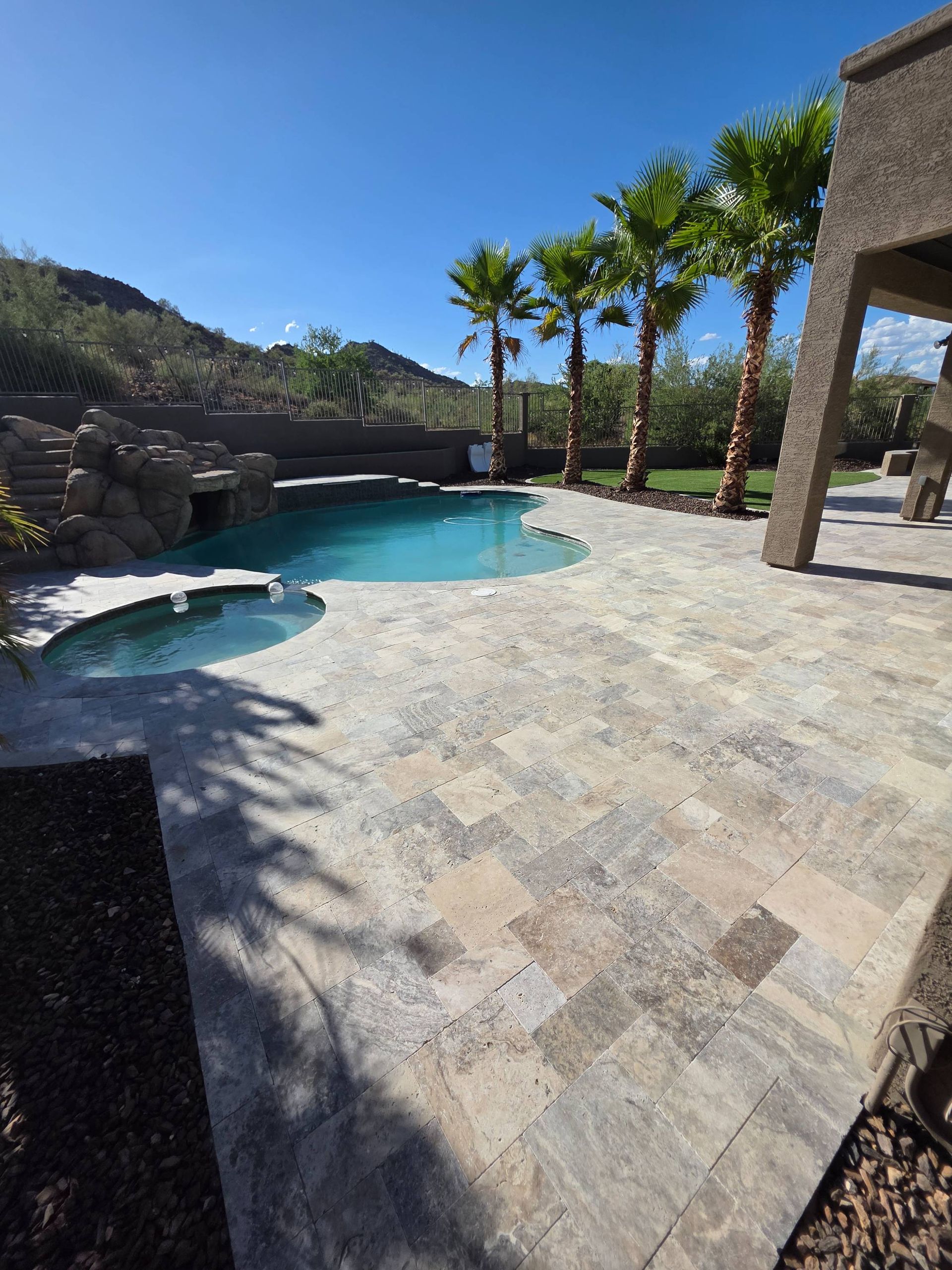 Patio with pool, palm trees, and mountain backdrop under a clear blue sky.