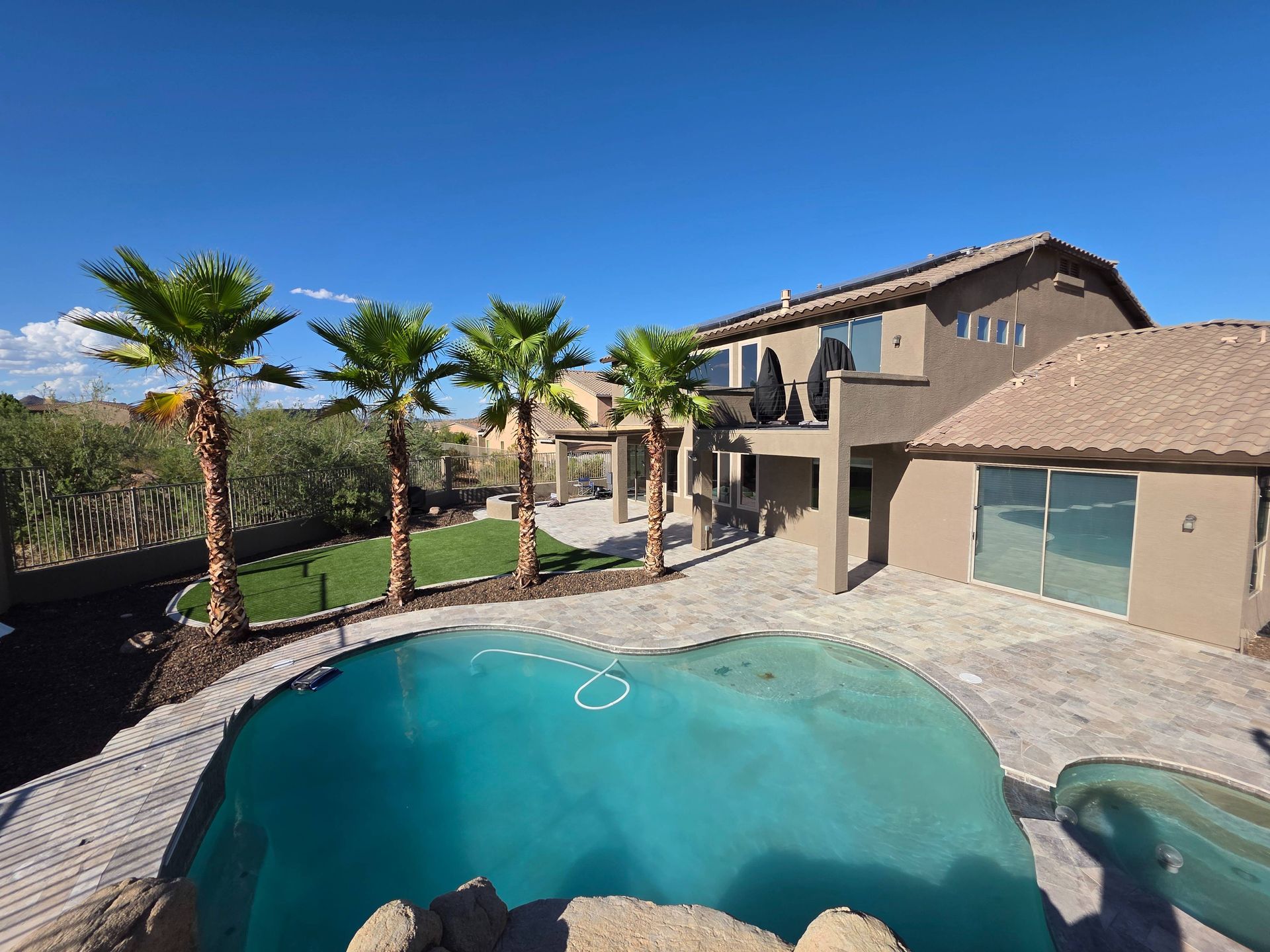 Backyard with pool, palm trees, and a two-story house under a clear blue sky.