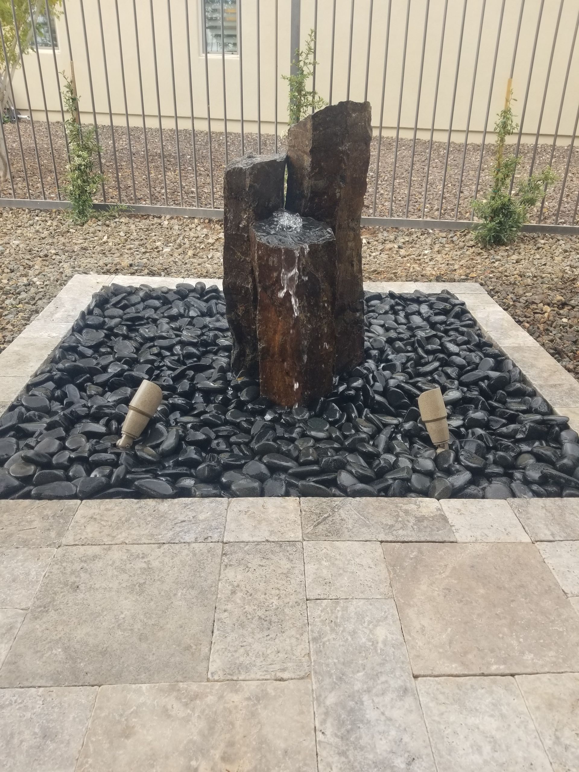 A fountain is surrounded by black rocks and a fence