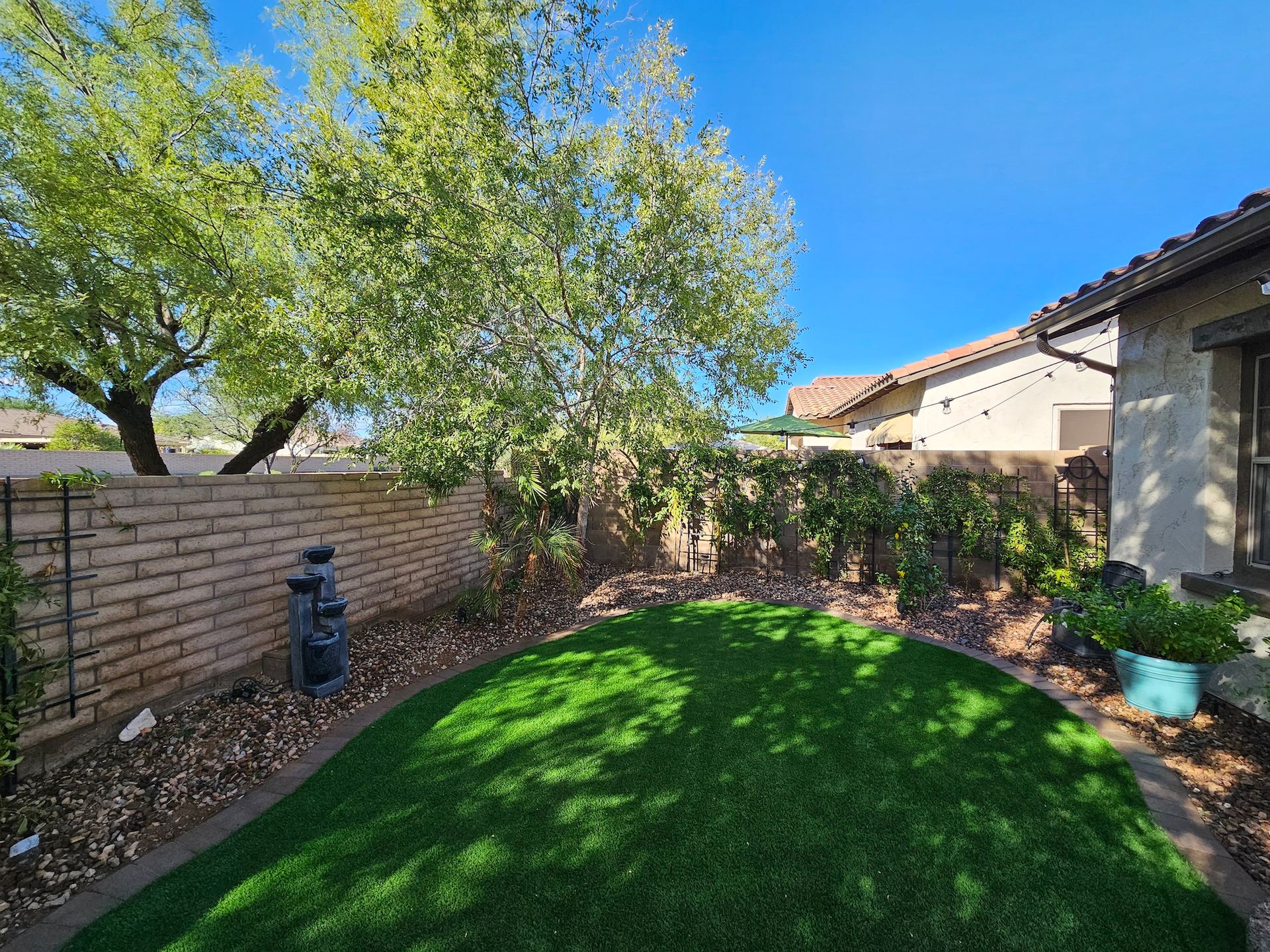 A backyard with a lush green lawn and a brick fence.