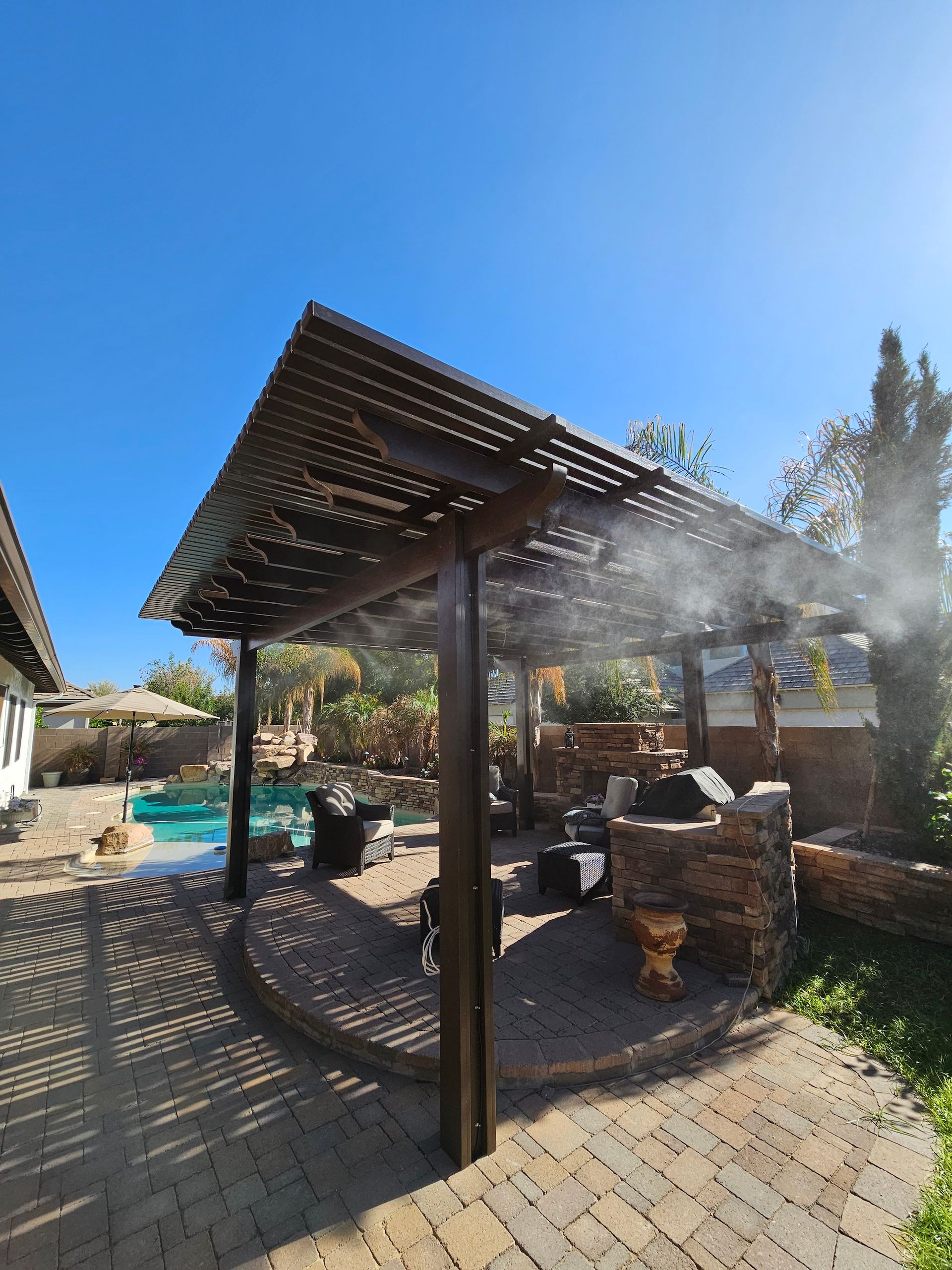 A patio with a pergola and a swimming pool in the background.