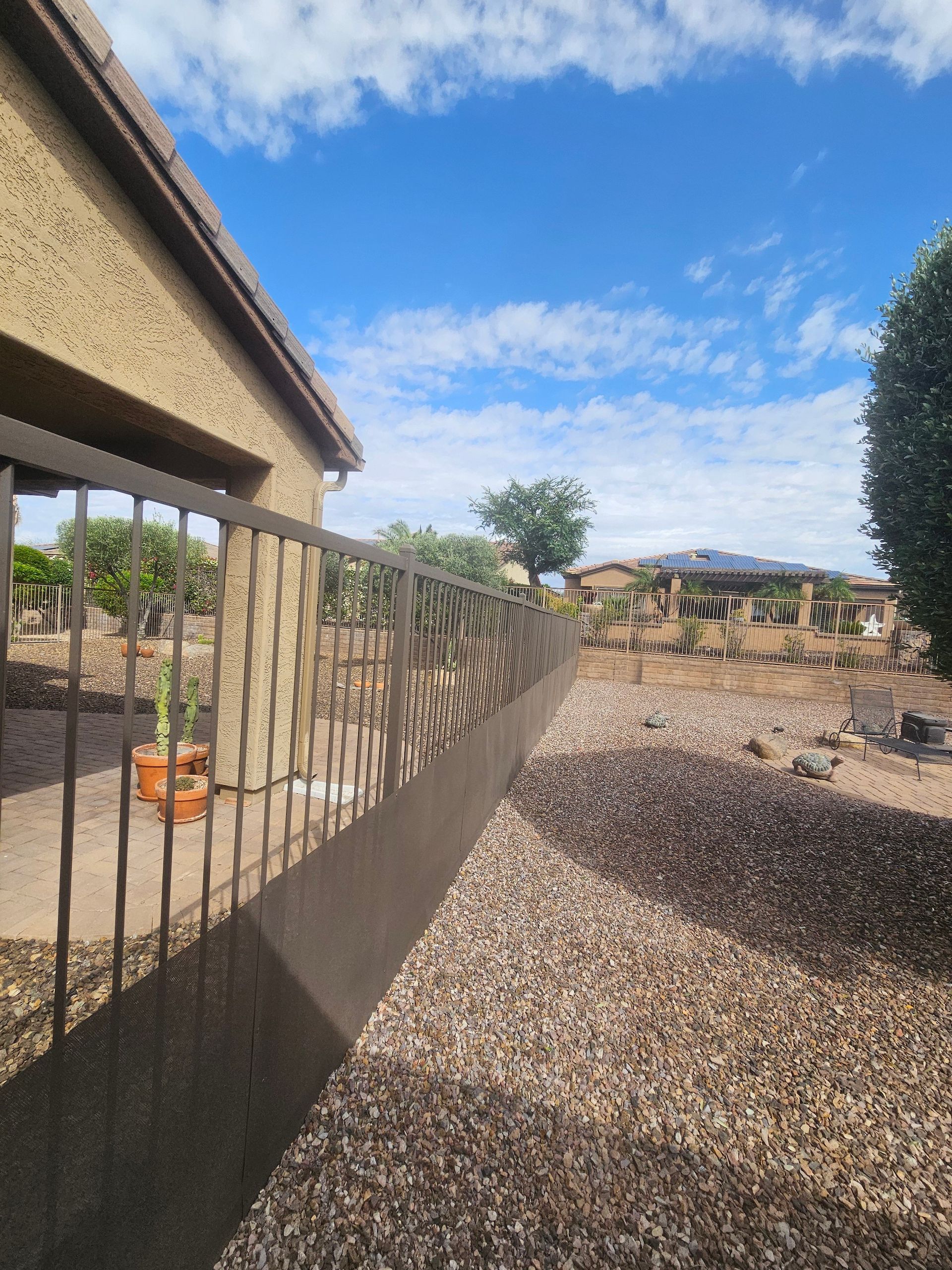 A fence with a house in the background and gravel in the foreground