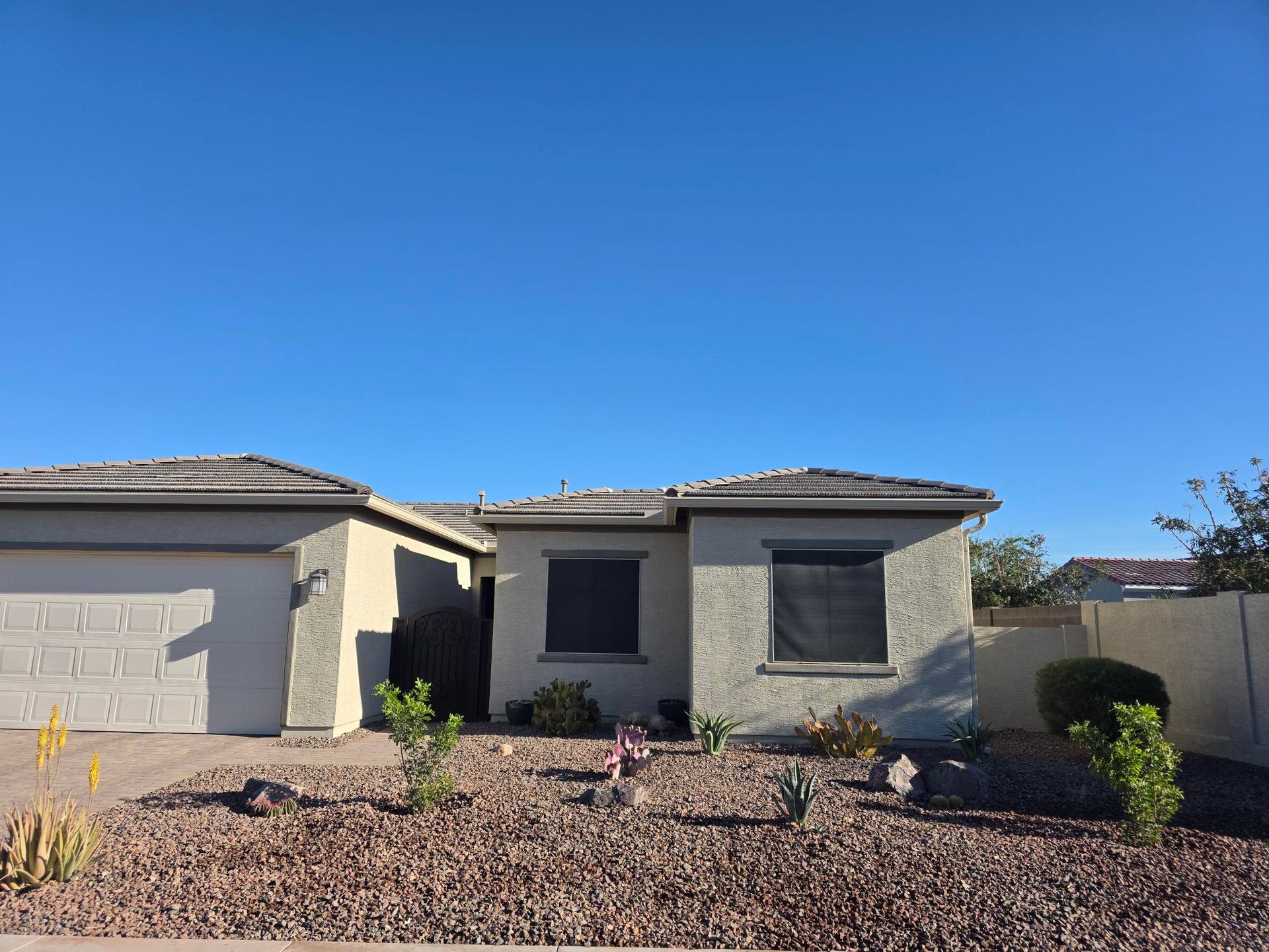 A single-story tan stucco house under a bright blue sky, with a front-loading garage and a desert-landscaped yard.