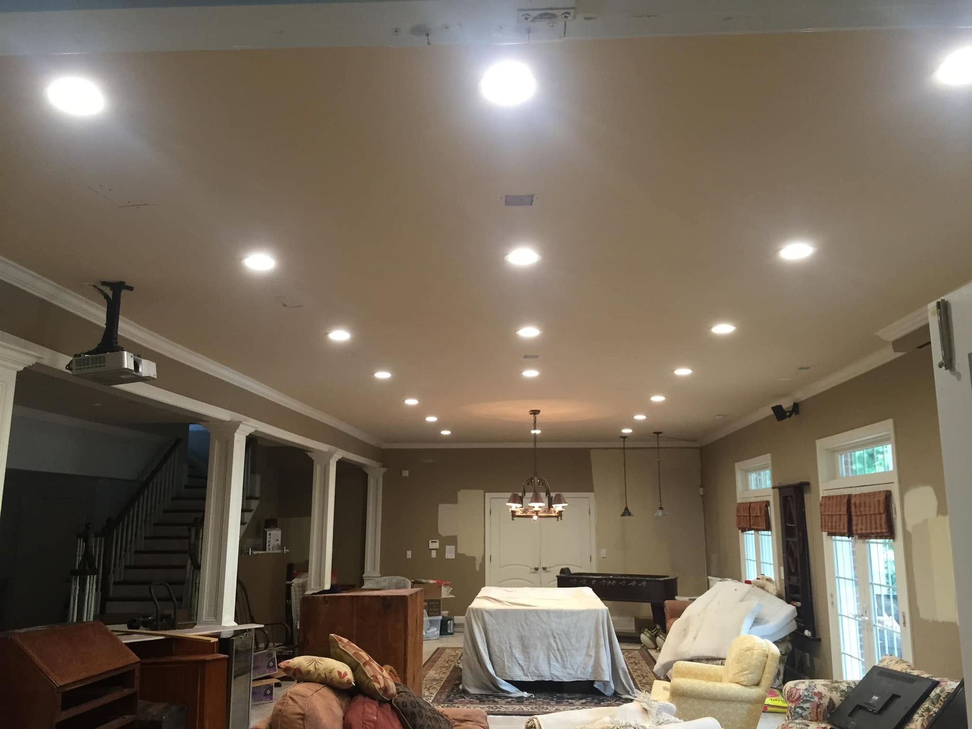 Spacious living room with recessed lights, staircase, covered furniture, and sliding glass doors.