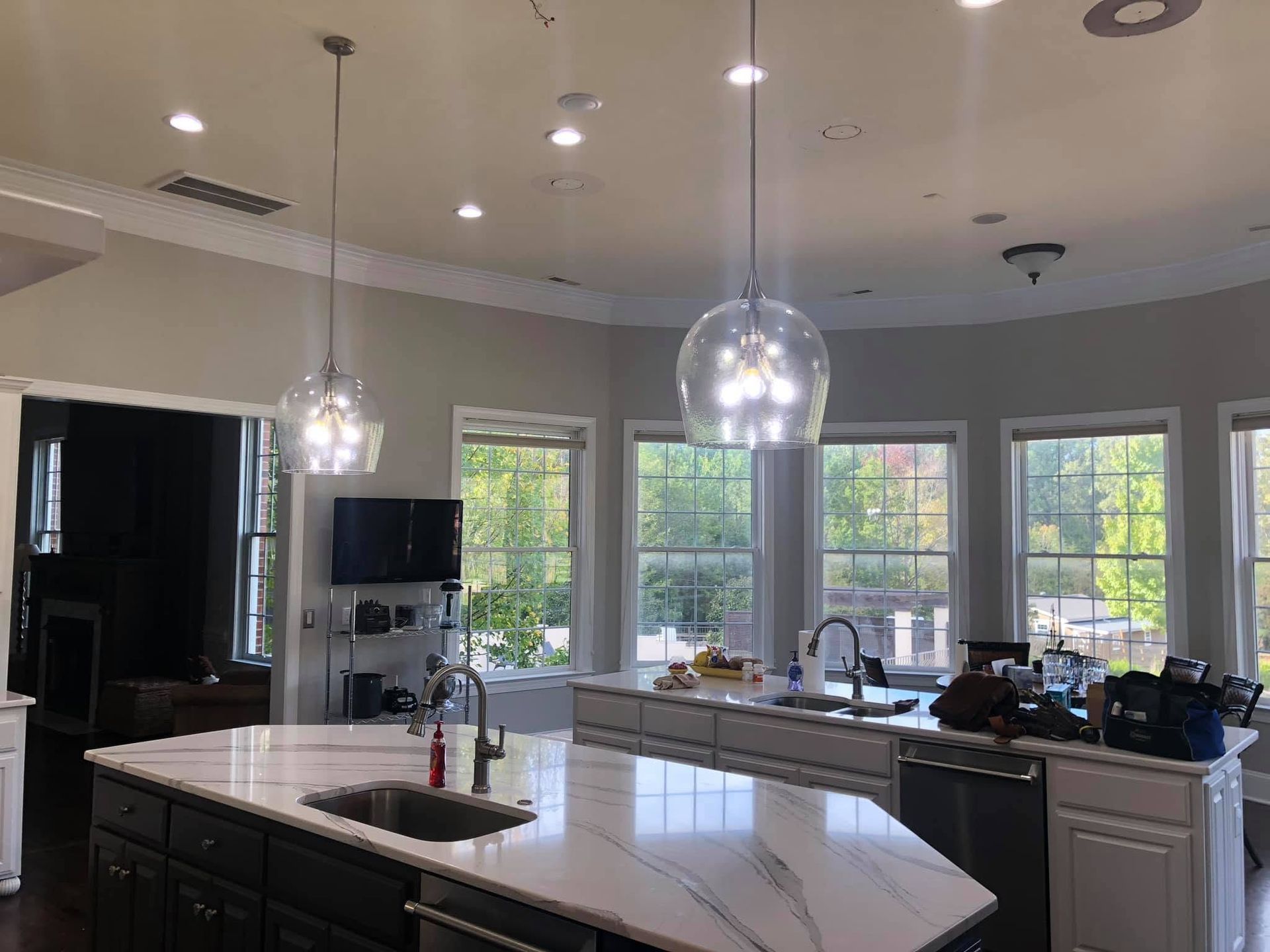 Bright modern kitchen with white island, pendant lights, and large windows overlooking greenery