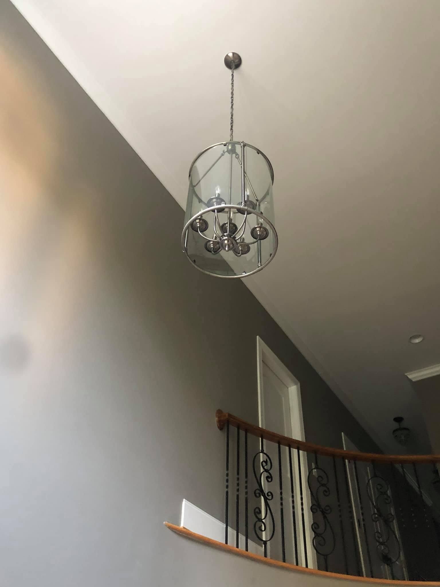 Chrome chandelier hanging in a stairwell with gray walls and a wooden banister