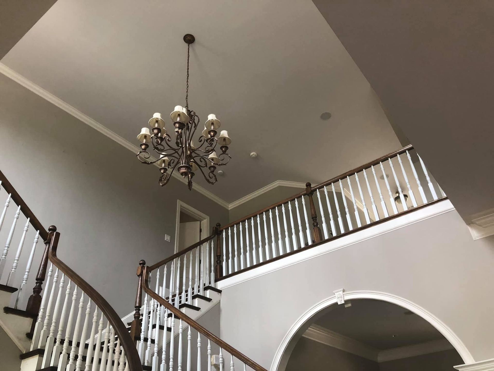 Grand foyer with chandelier, staircase, and arched entryway in a neutral-toned home