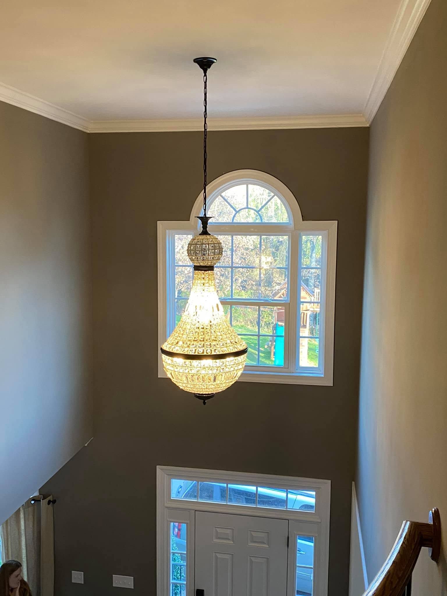 Stairwell with hanging chandelier, arched window, and white front door below.