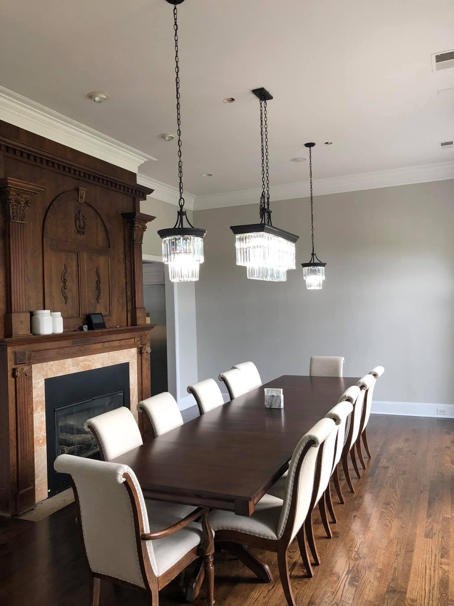 Elegant dining room with long dark wood table, white chairs, hanging lights, and fireplace mantle