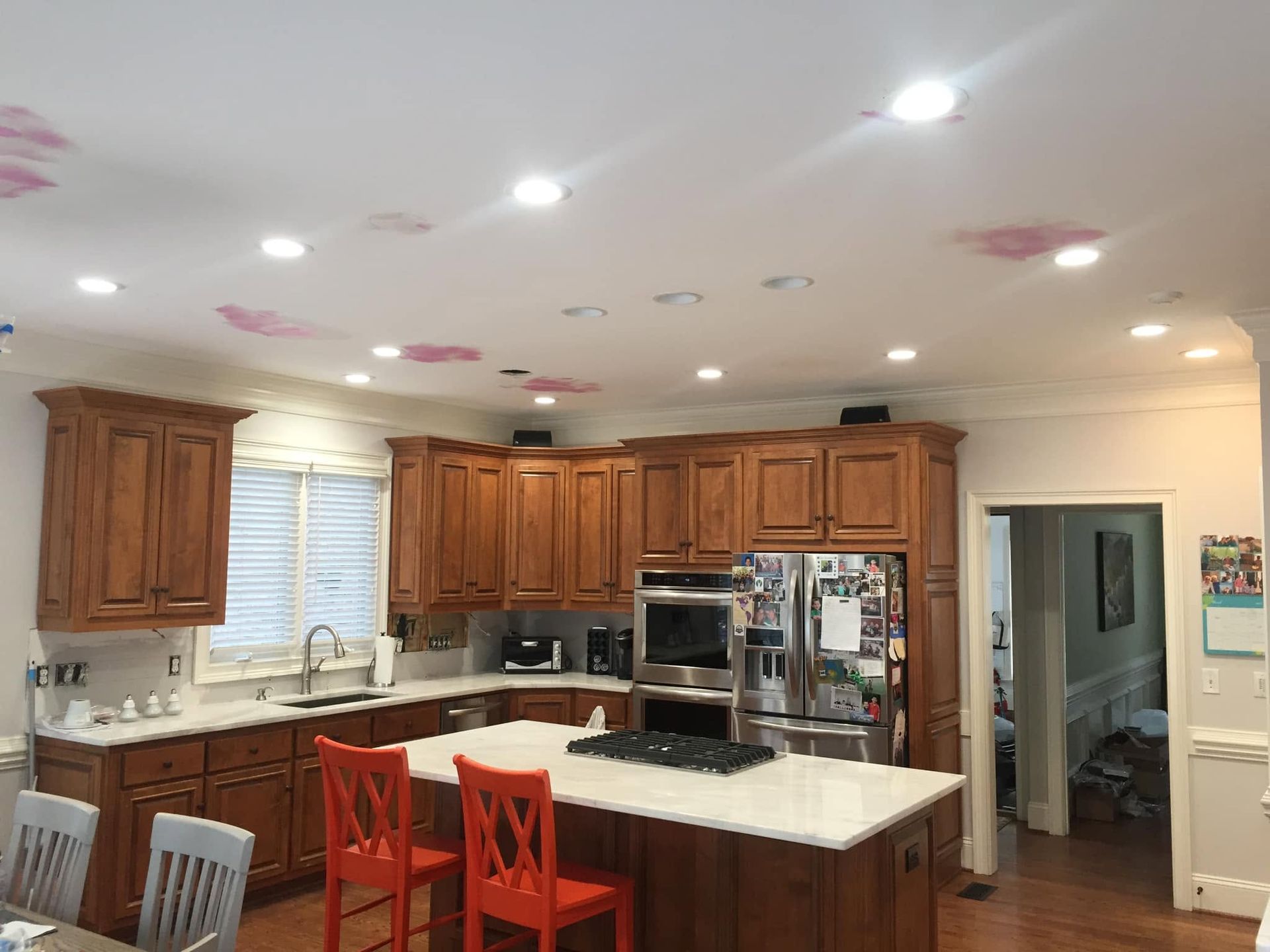 Modern kitchen with wooden cabinets, white countertops, island stools, and stainless steel appliances