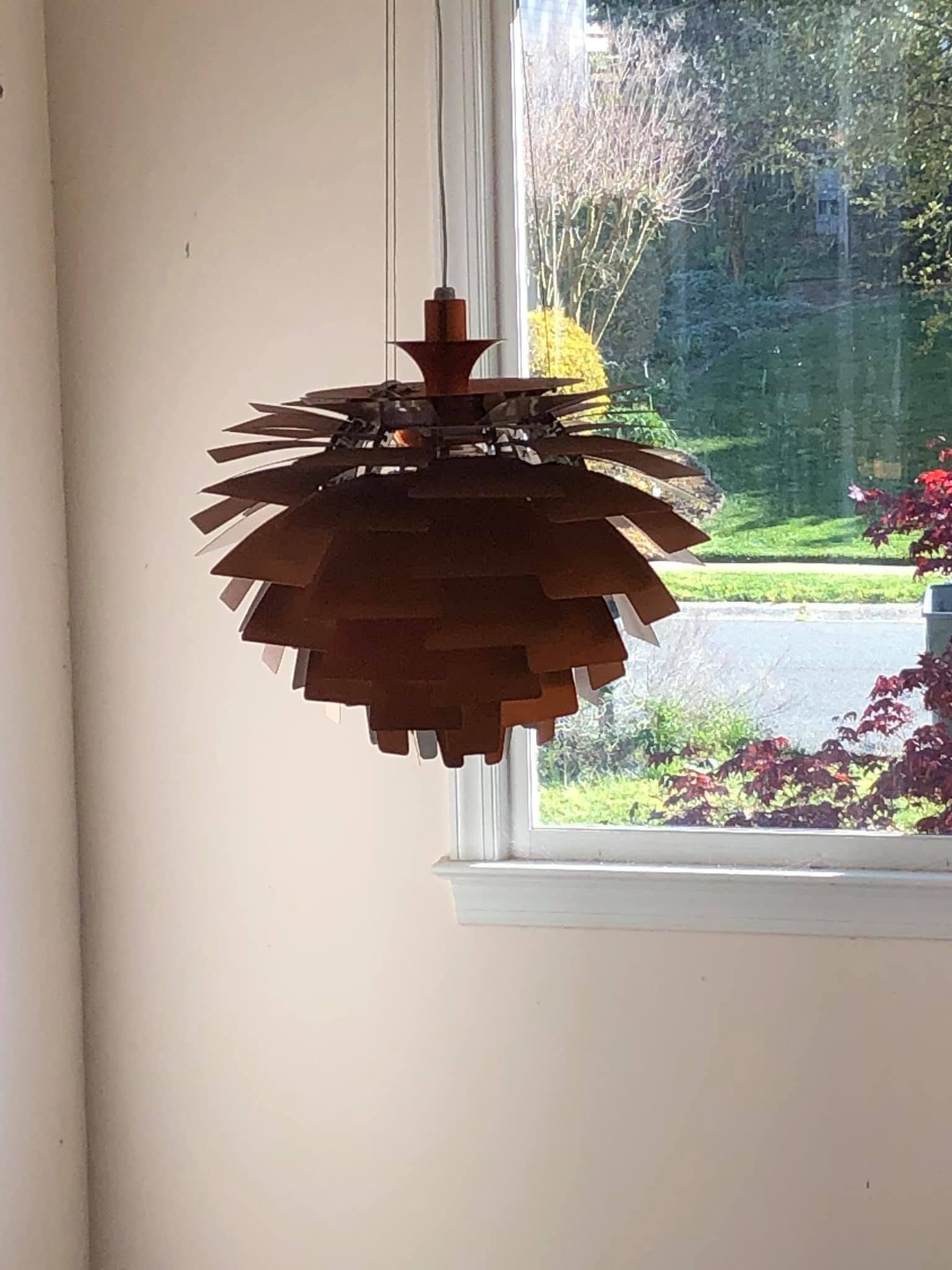 Wooden pendant light hanging by a window, with daylight and garden view outside.