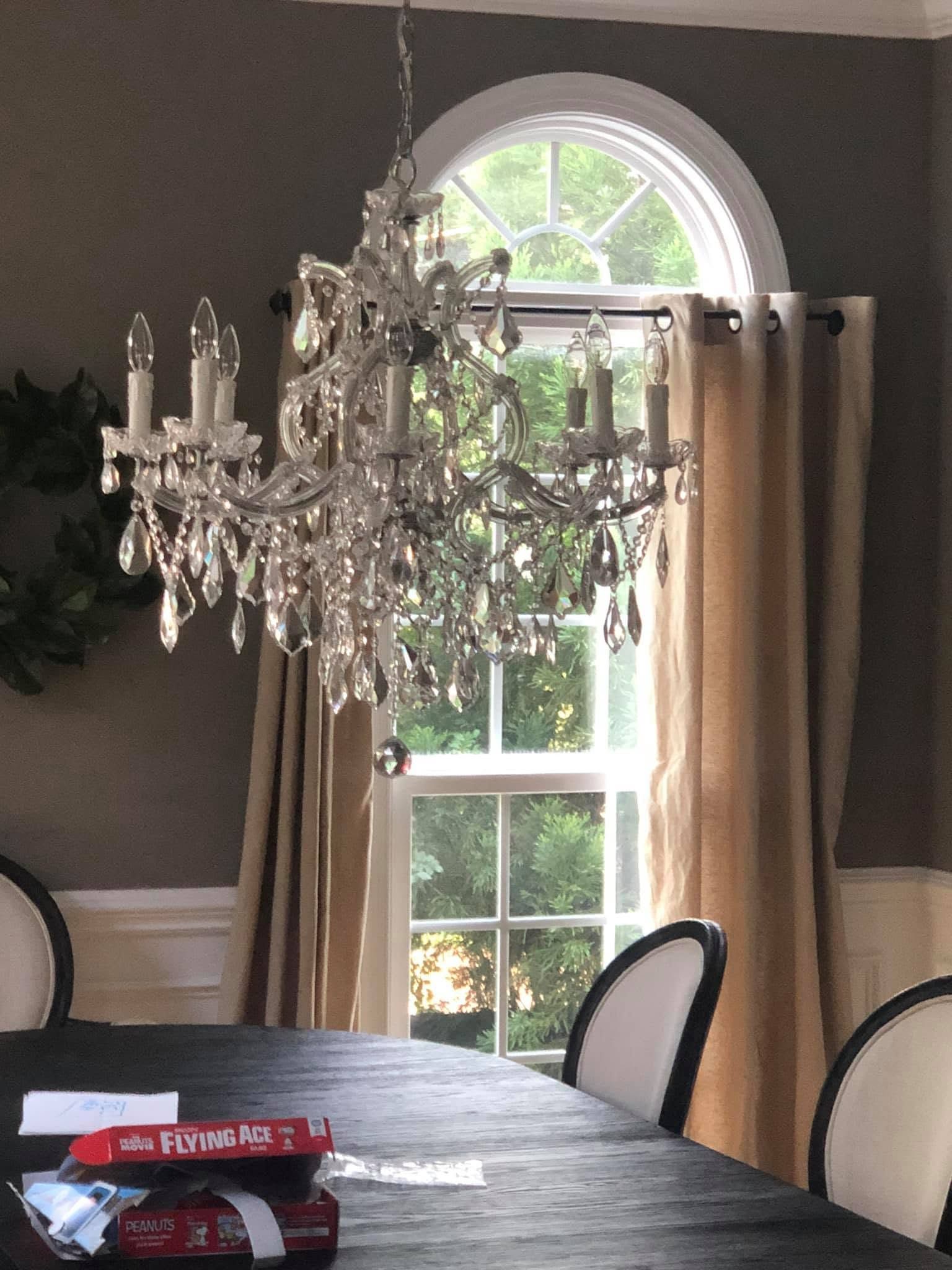 Dining room with a chandelier, arched window, beige curtains, and a table with red napkins.