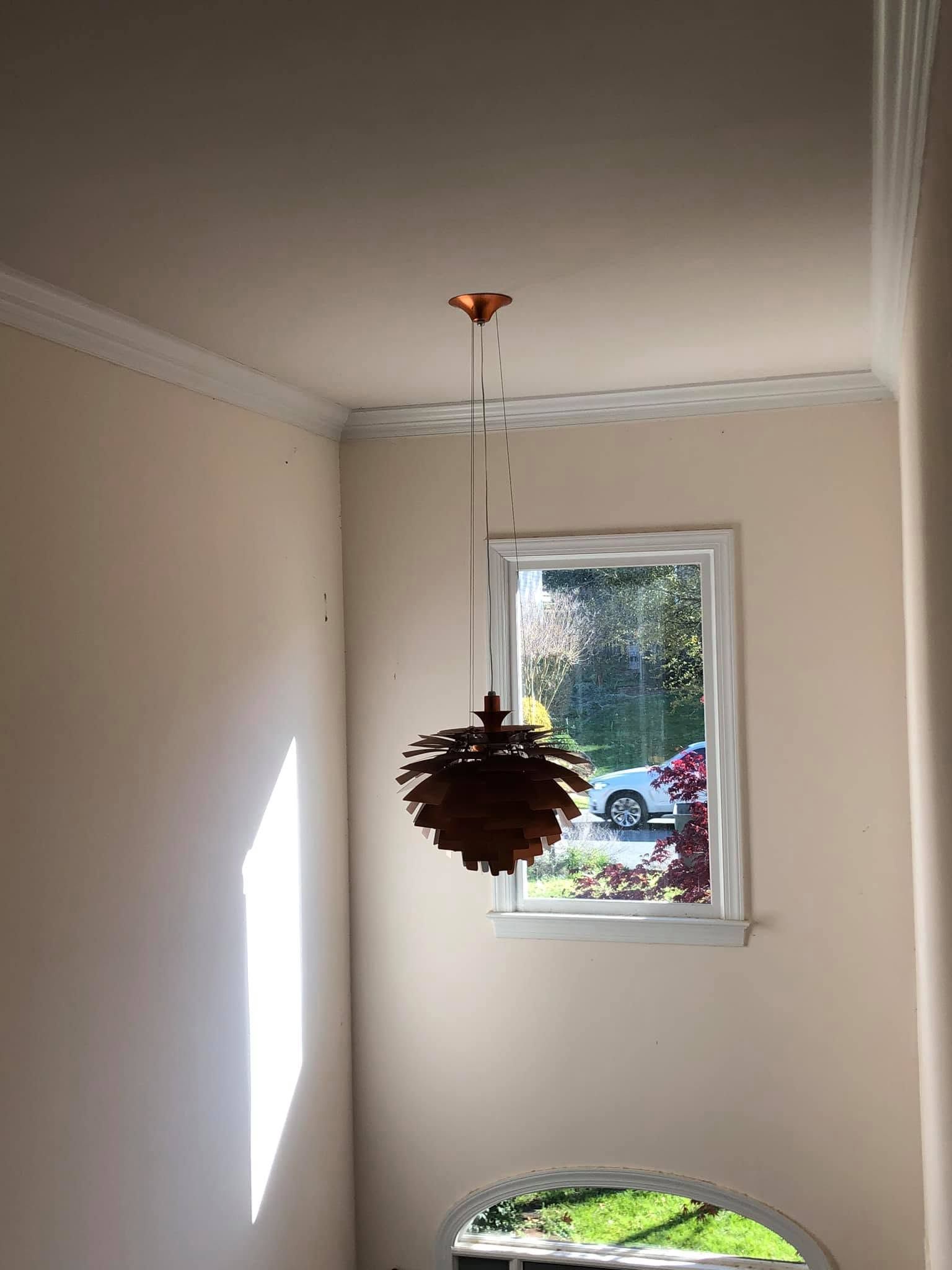 Narrow beige stairwell with a window and hanging pinecone light fixture, sunlight on the left wall.