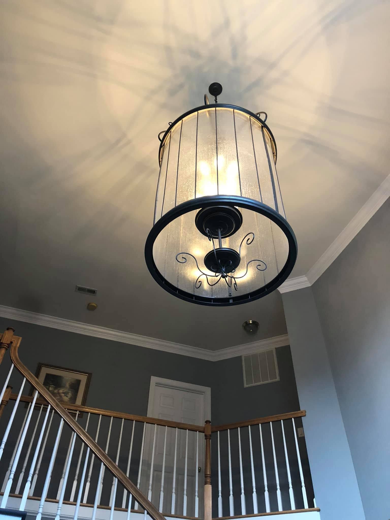 Large black chandelier hanging in a stairwell with gray walls and white railings
