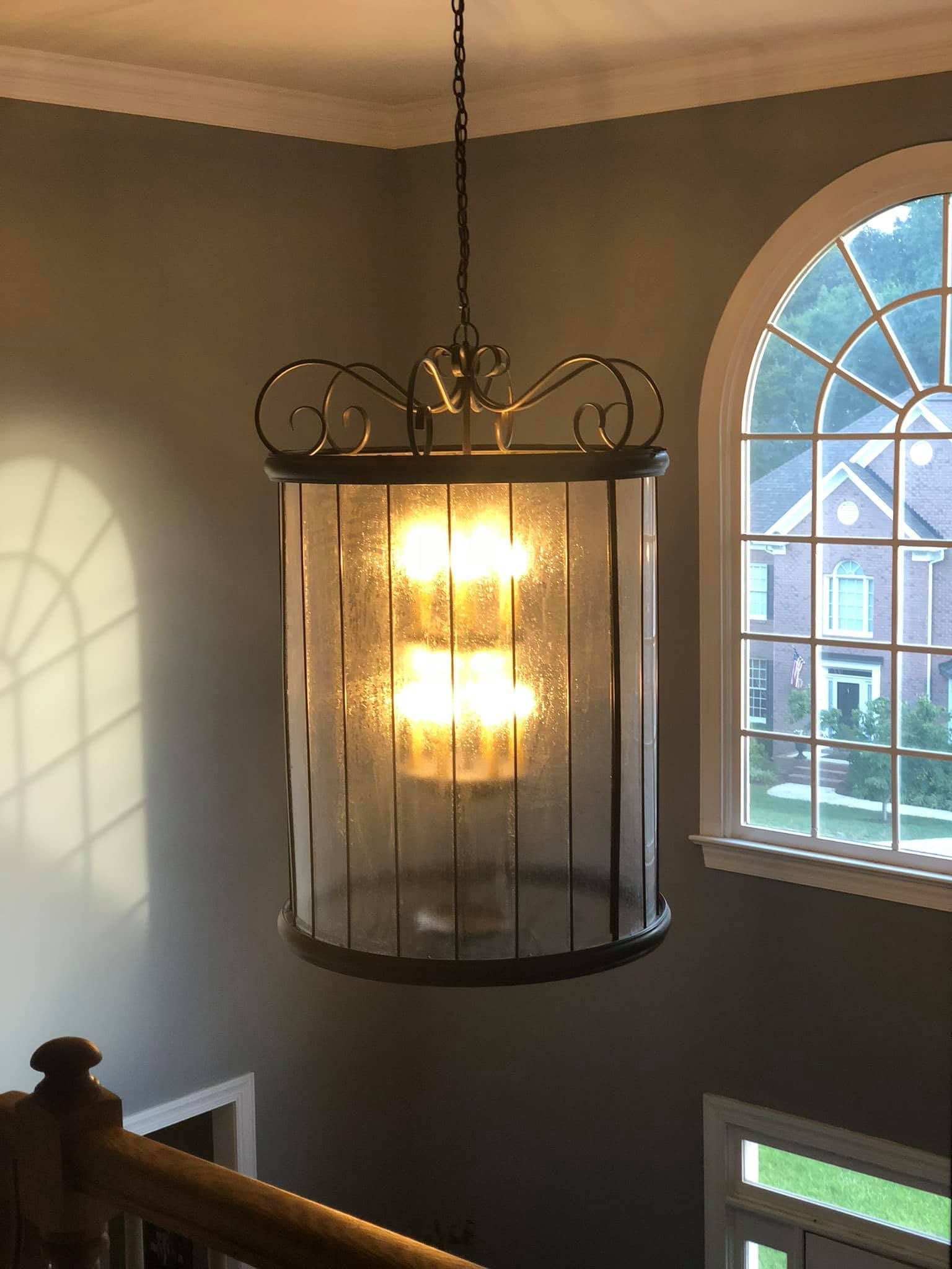 Indoor staircase with a hanging chandelier beside an arched window, lit by warm light.