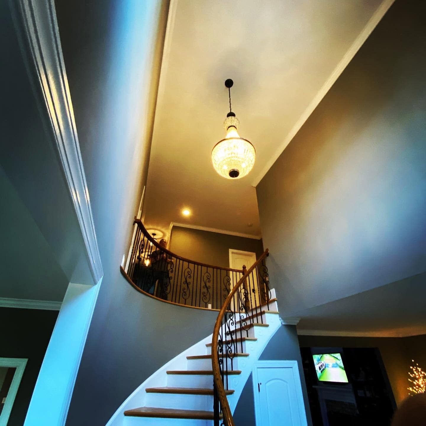 Curved staircase in a modern home hallway with a hanging chandelier and warm lighting