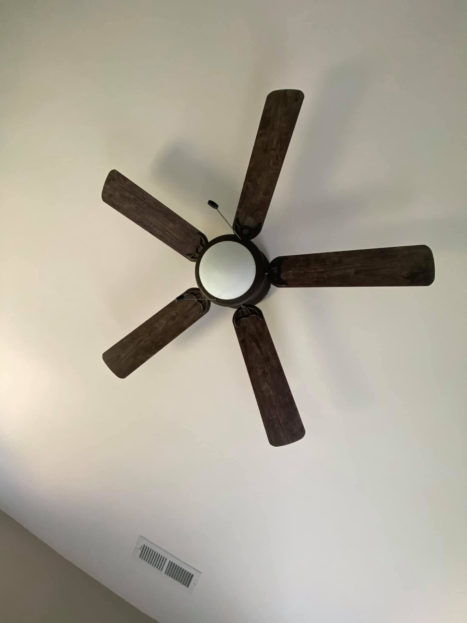 Ceiling fan with five dark blades and a round light fixture on a white ceiling